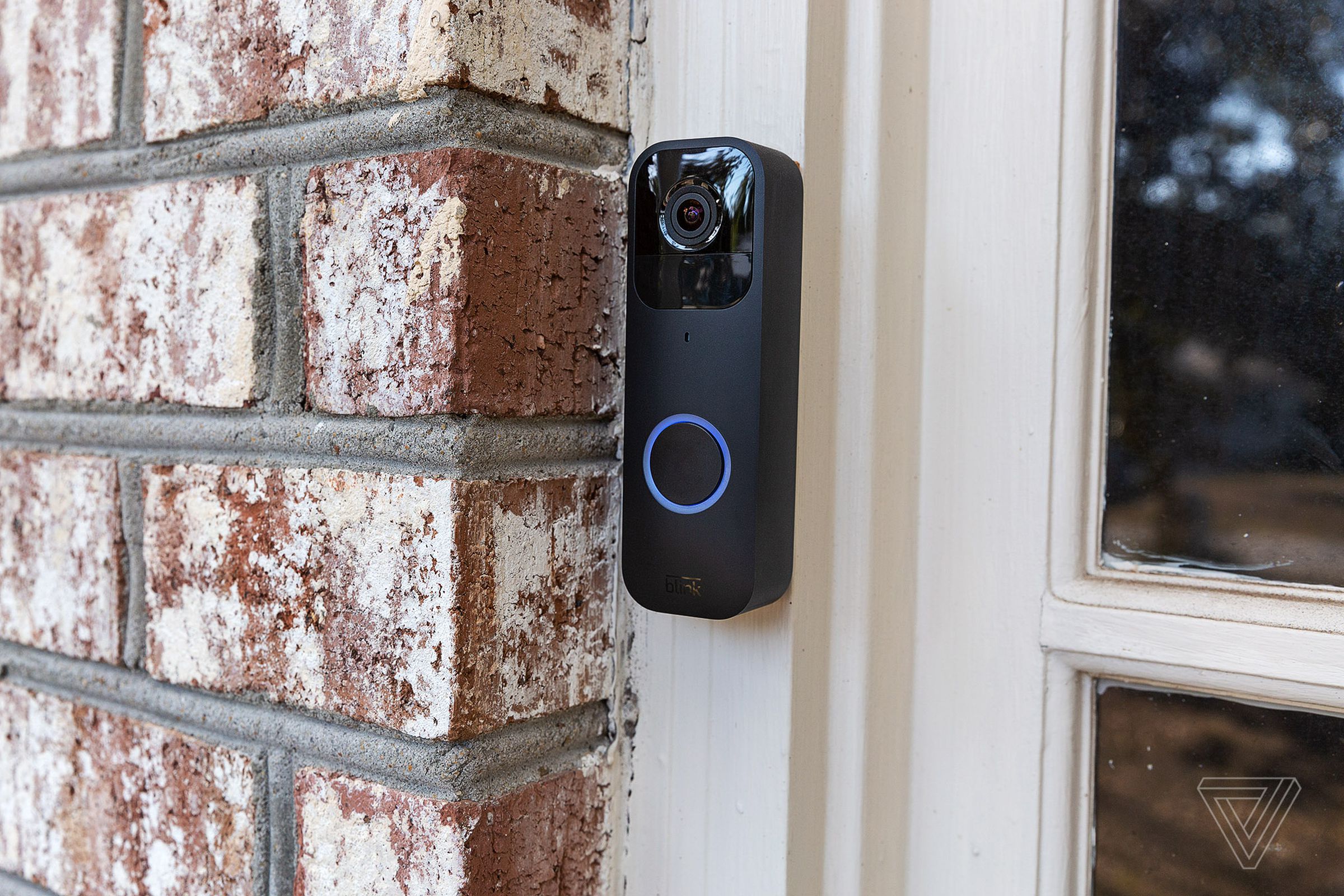 The black Blink Video Doorbell hung up on a brick wall outside of a house.