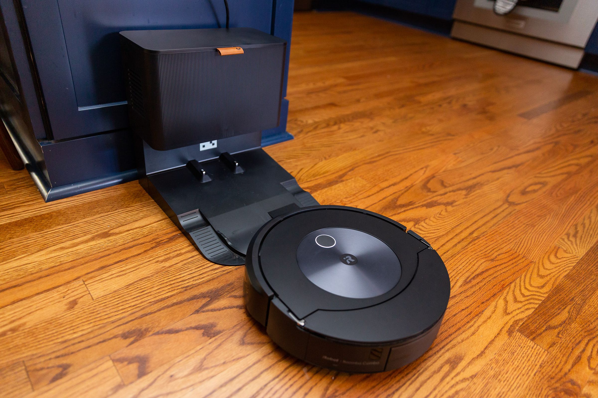 Photo of the Roomba Combo J7 approaching its auto-empty base. The base is about the size of a small kitchen trash can.