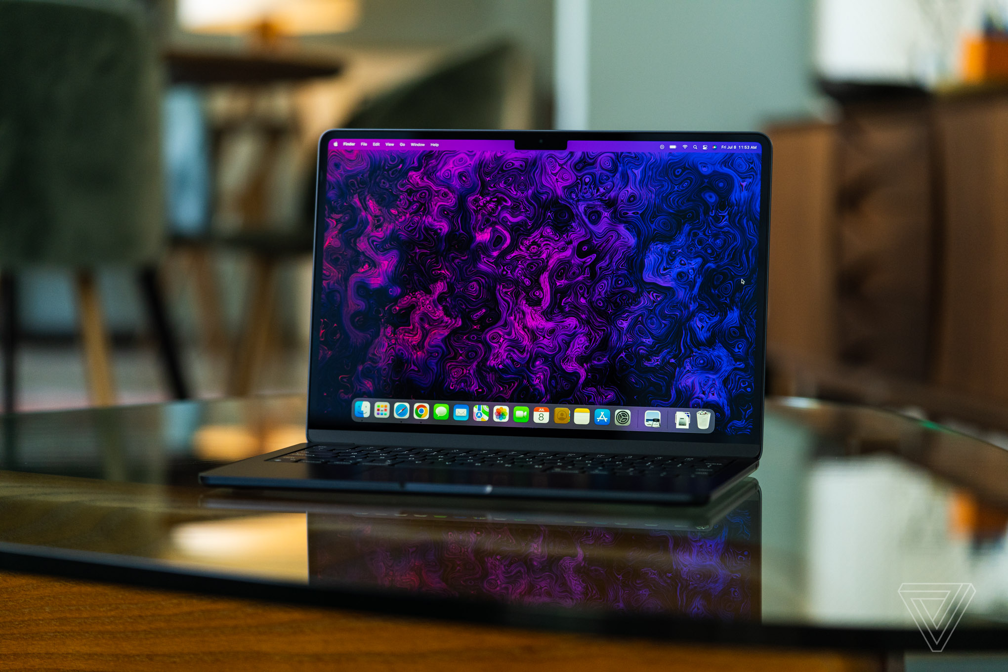 The M2 MacBook Air is opened, facing the camera. Its display is on, showcasing a psychedelic purple and black wallpaper created by The Verge’s art and illustration team.