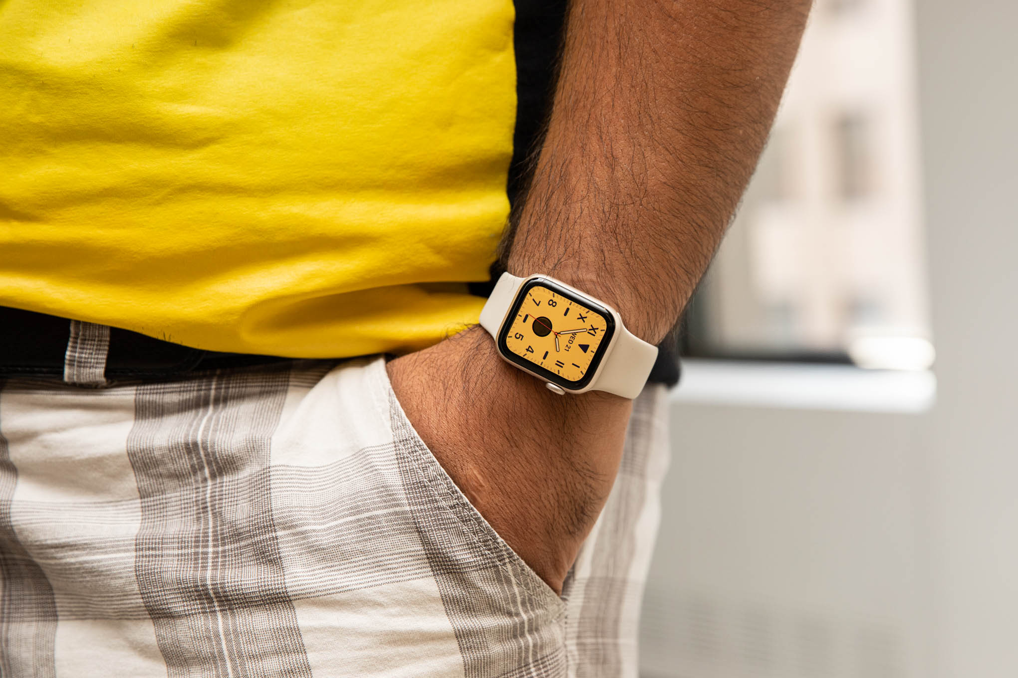 Man in yellow shirt with hand in pocket wearing second gen Apple Watch SE with a yellow watchface