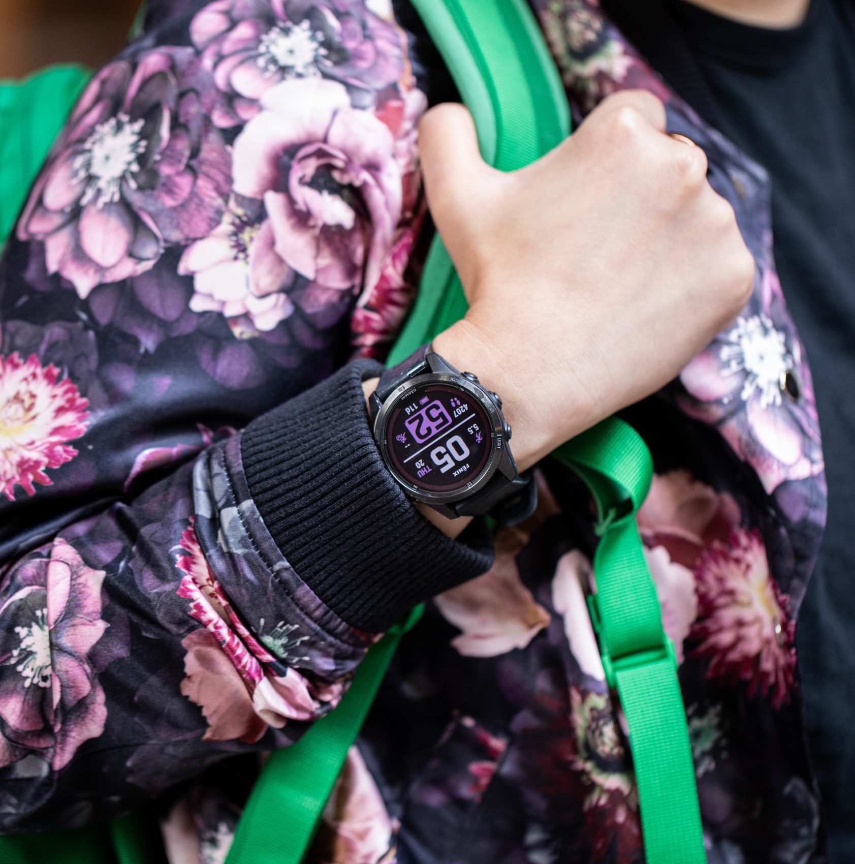 Person wearing a floral jacket and bright green backpack with a Garmin Fenix 7S Pro on their wrist