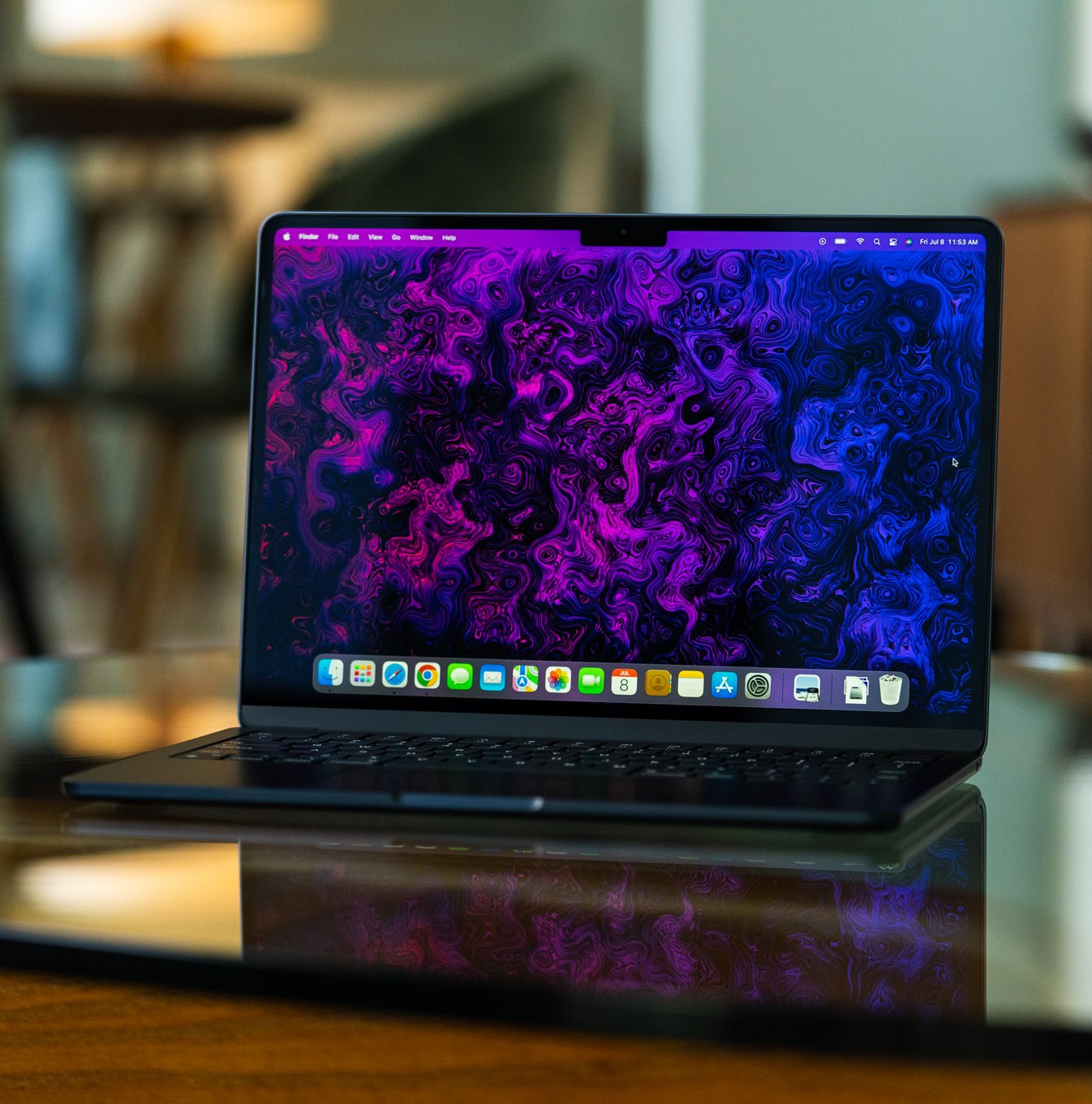 The M2 MacBook Air is opened, facing the camera. Its display is on, showcasing a psychedelic purple and black wallpaper created by The Verge’s art and illustration team.