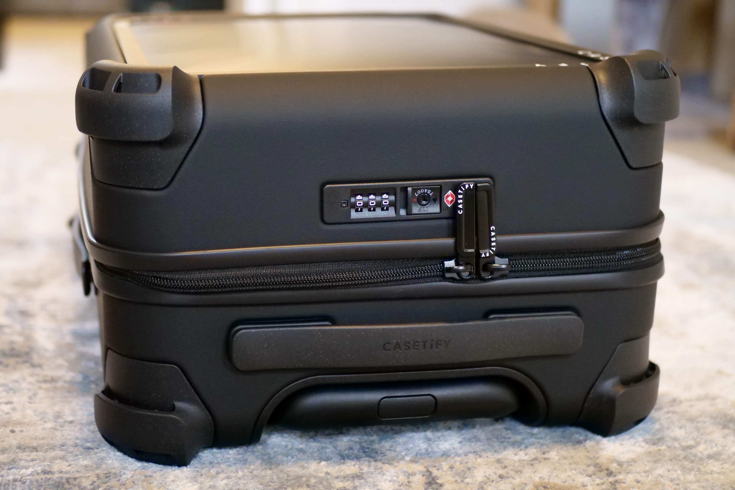 The lock, extendable handle, and zip on the Casetify Carry-On Suitcase.