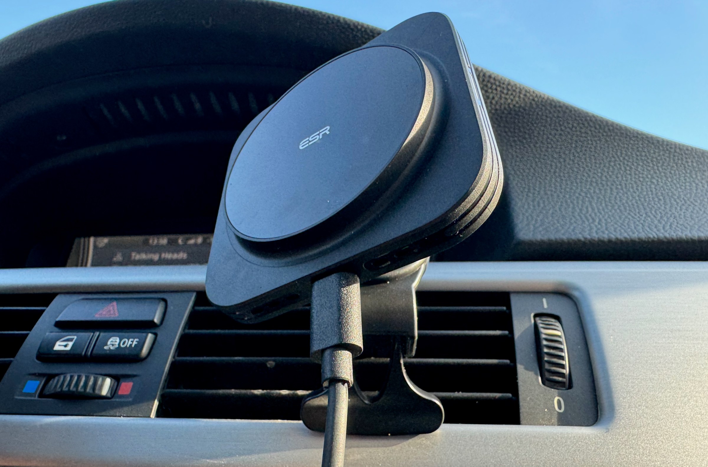 A black plastic car charging mount with the ESR logo at the center of the circular charging puck is mounted to a car’s vent.