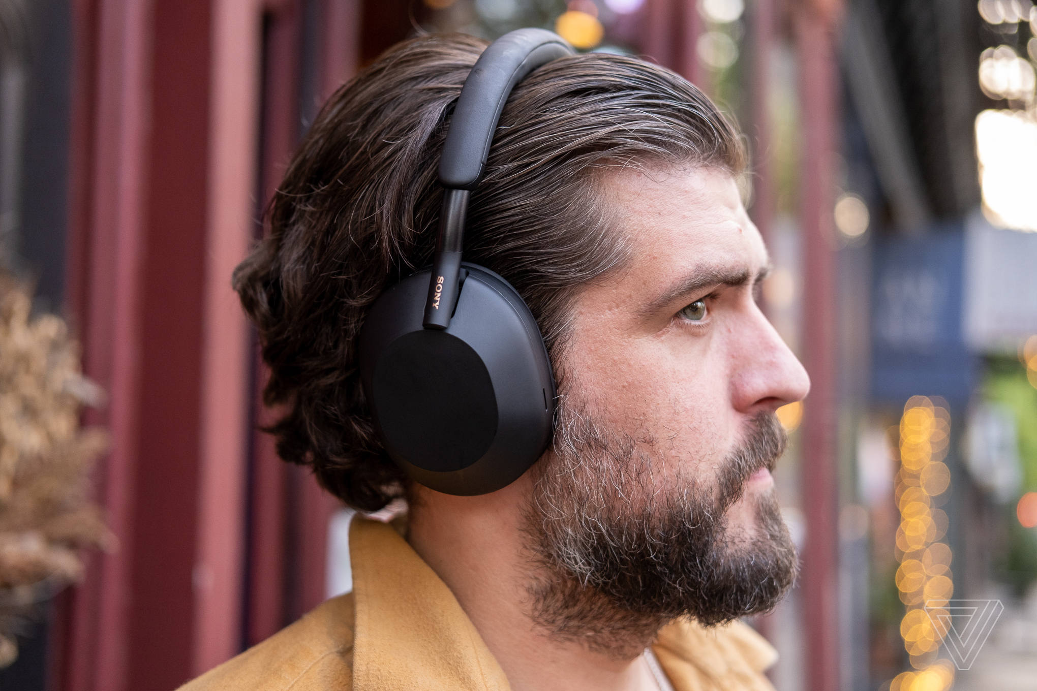 A man wearing Sony’s black WH-1000XM5 noise-canceling headphones outside.