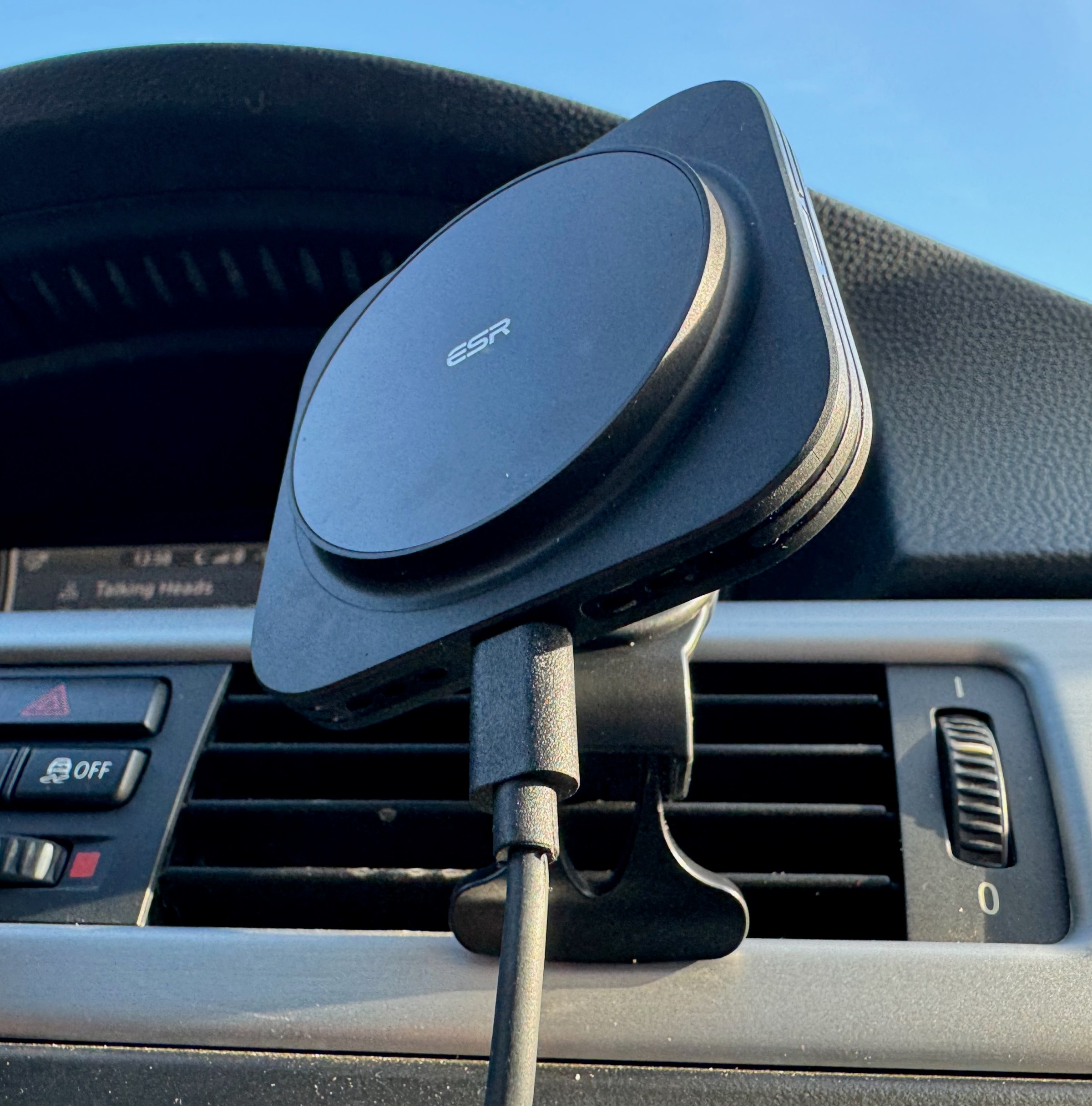 A black plastic car charging mount with the ESR logo at the center of the circular charging puck is mounted to a car’s vent.