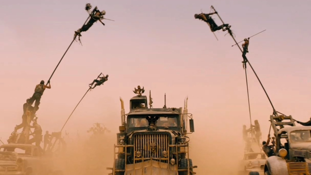 Men swing from poles while driving cars in the desert in