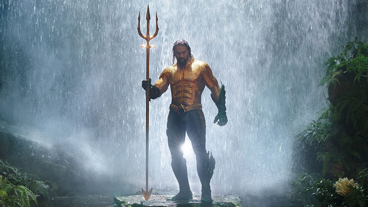 Aquaman standing in front of a waterfall holding a trident in the movie