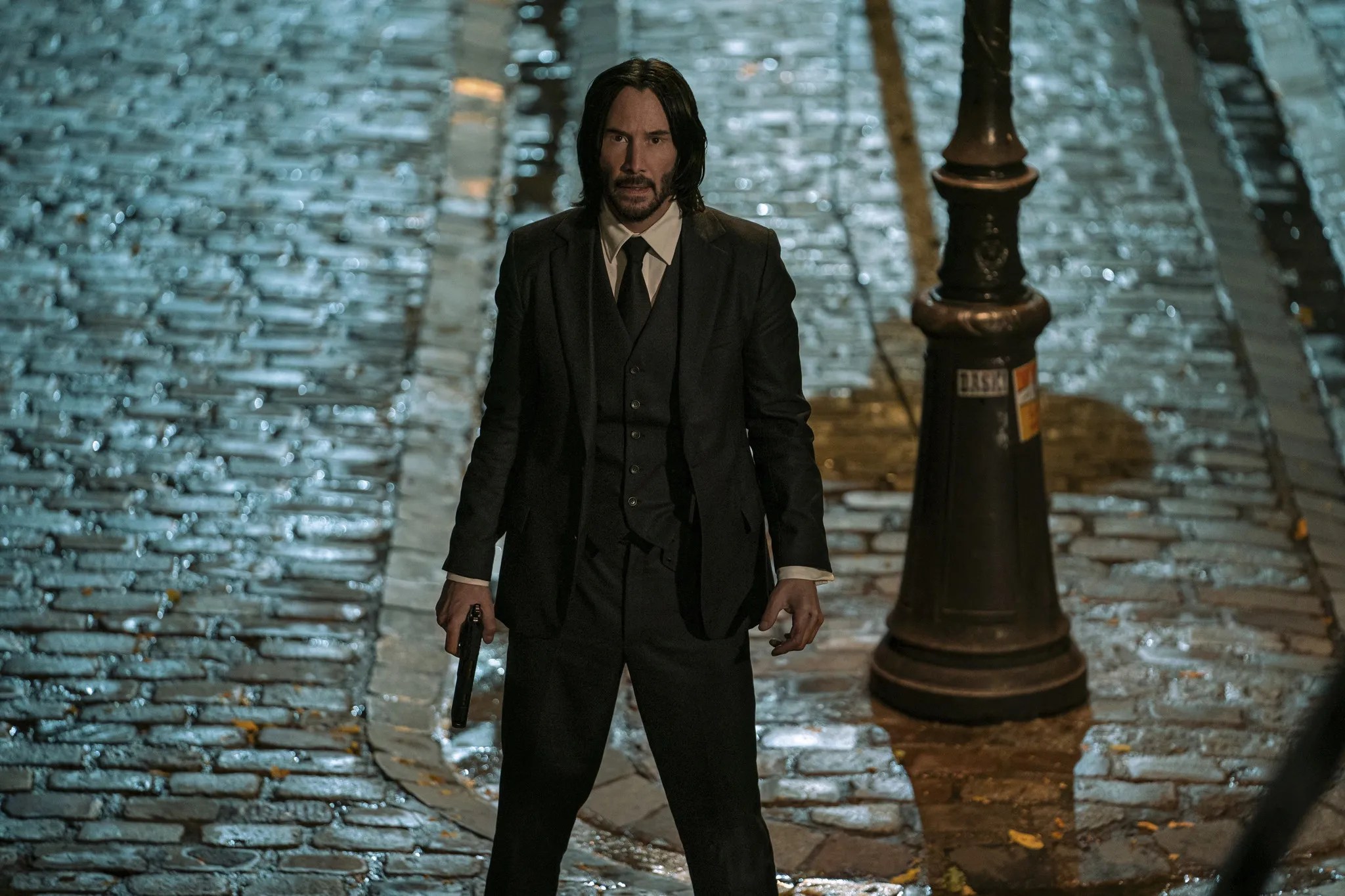 John Wick stands at the bottom of the stairs in