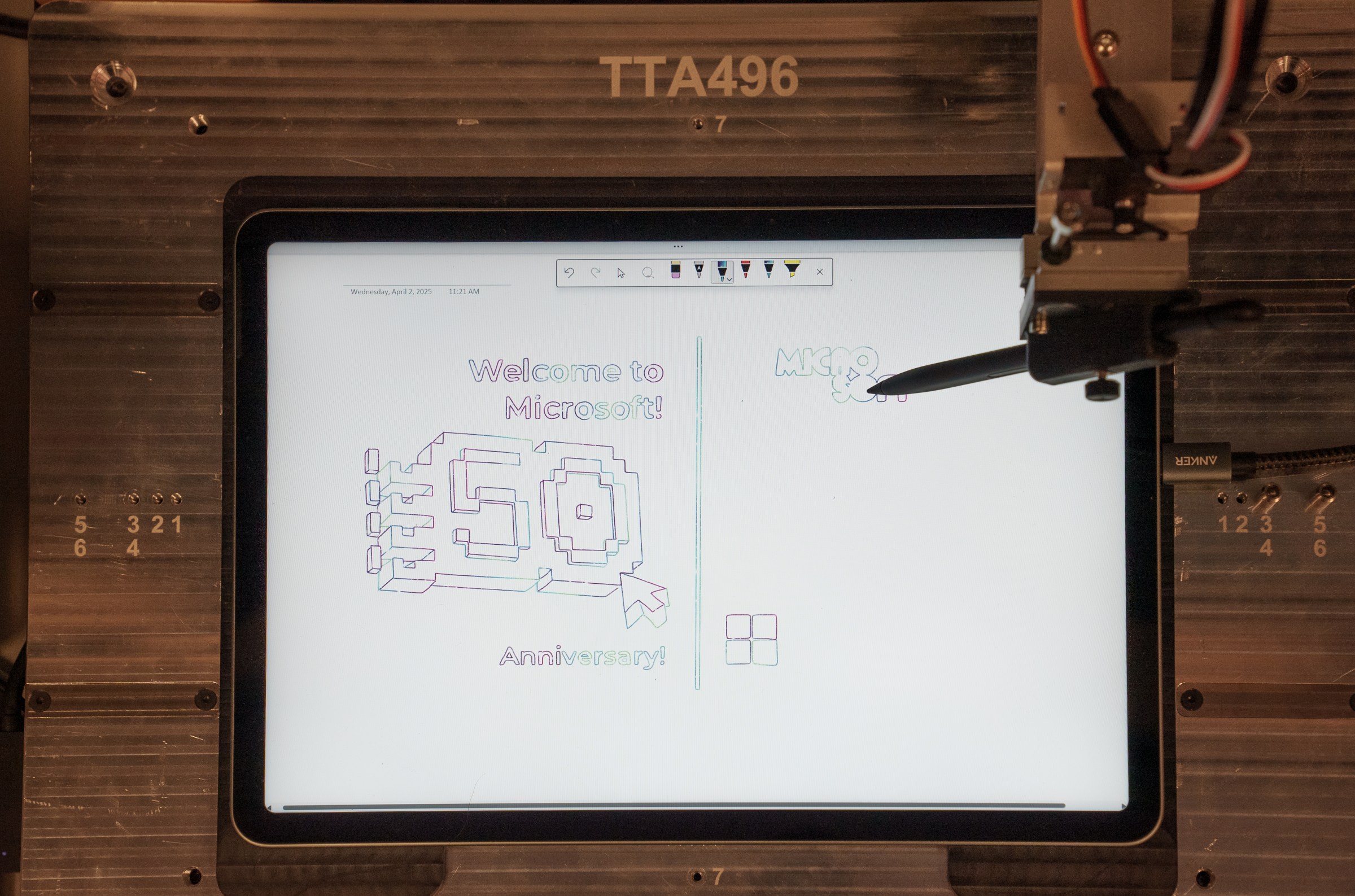 A robot creates a sketch of Microsoft’s 50th anniversary logo on a Surface Pro tablet.