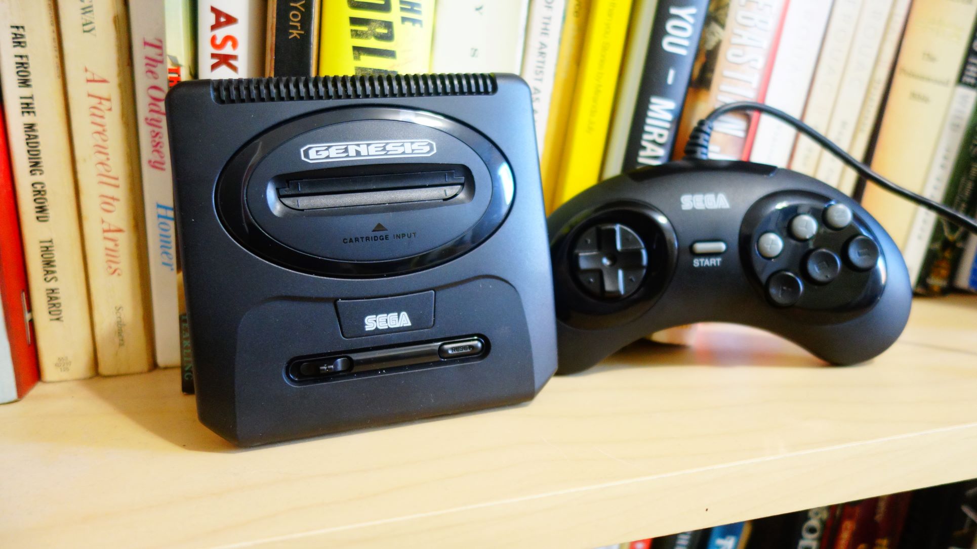 A Sega Genesis Mini 2 and its controller sit on a bookshelf.