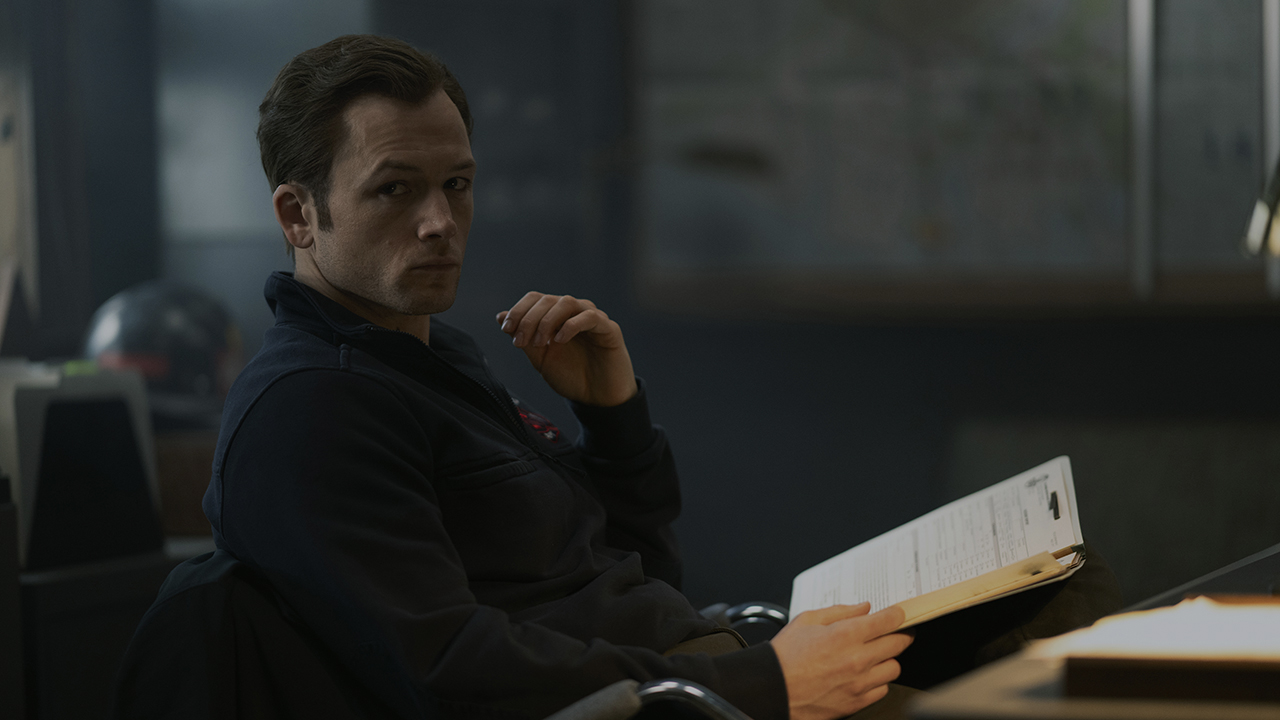 Taron Egerton sitting in a chair looking back in Smoke.