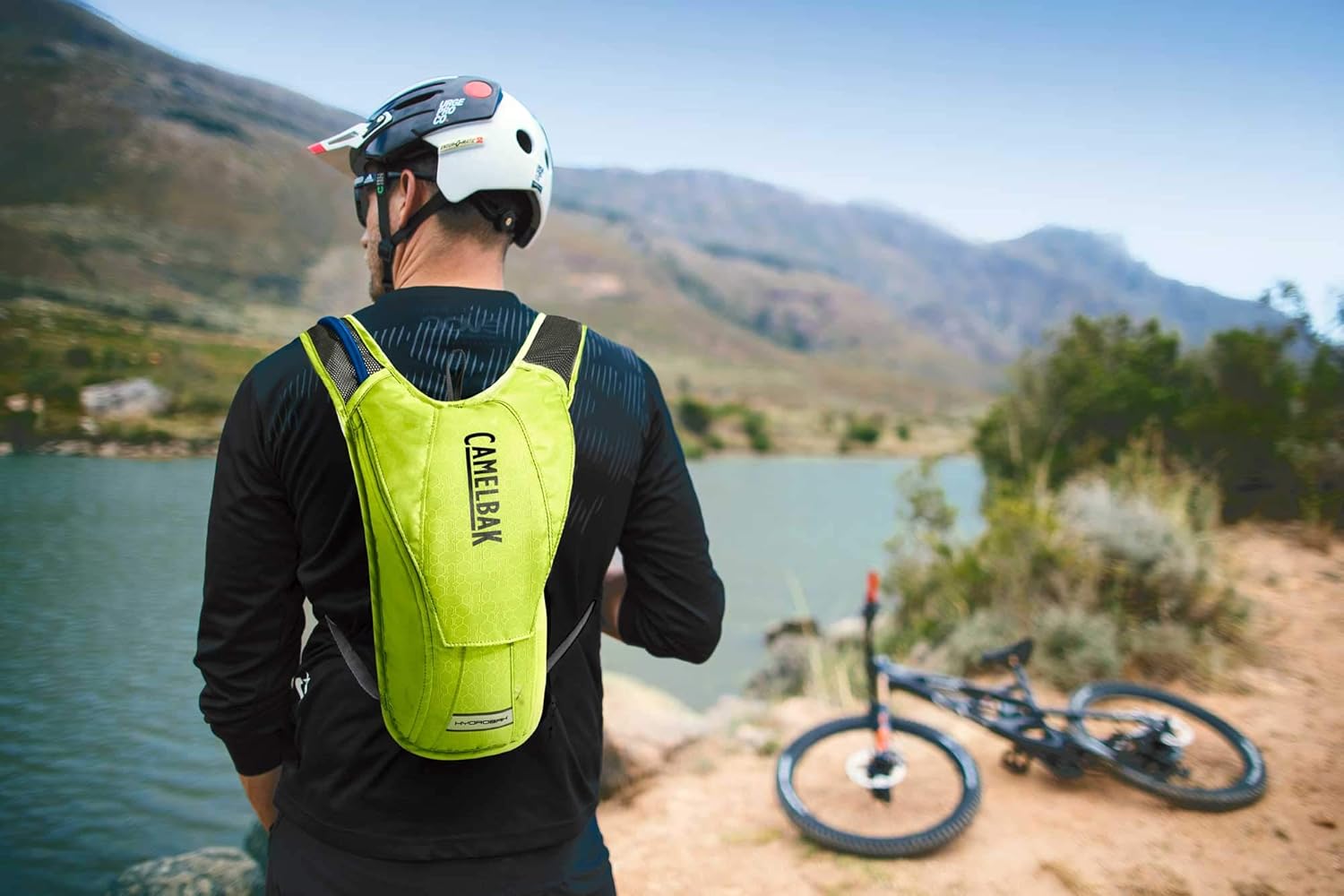 Biker rider wearing backpack with river and bike in background