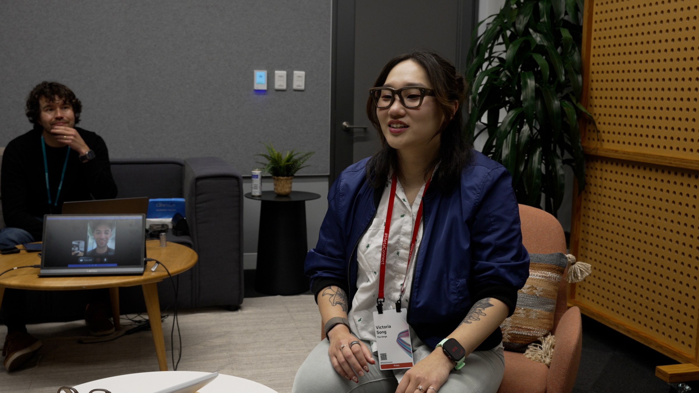 Image of Senior Reviewer Victoria Song sitting in a chair, looking down, but in the background you can see Senior Reporter Ja Peters on a screen 