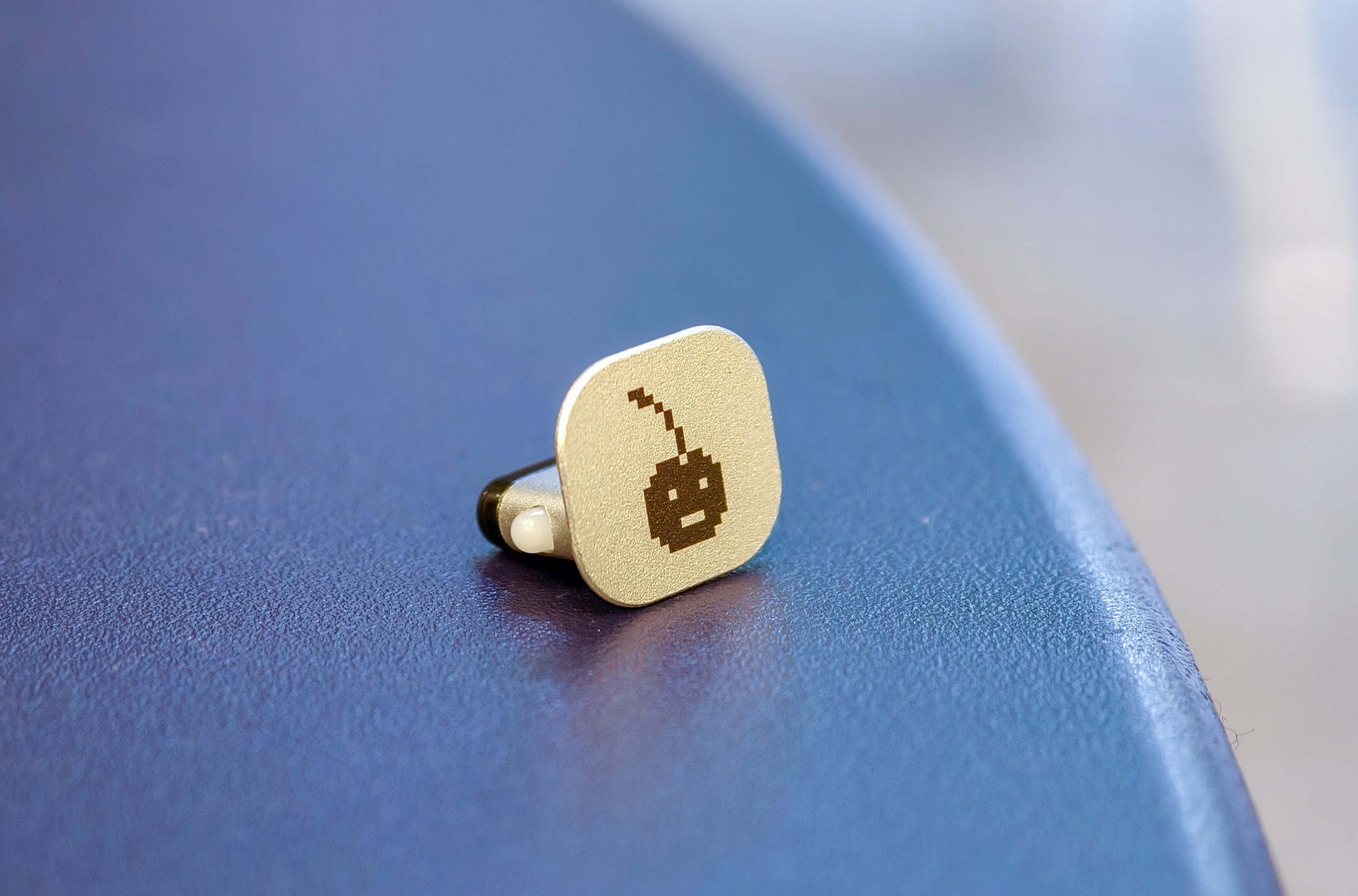 Ledger Nano Gen5 badge with a cherry icon designed by Susan Kare, lying on a table