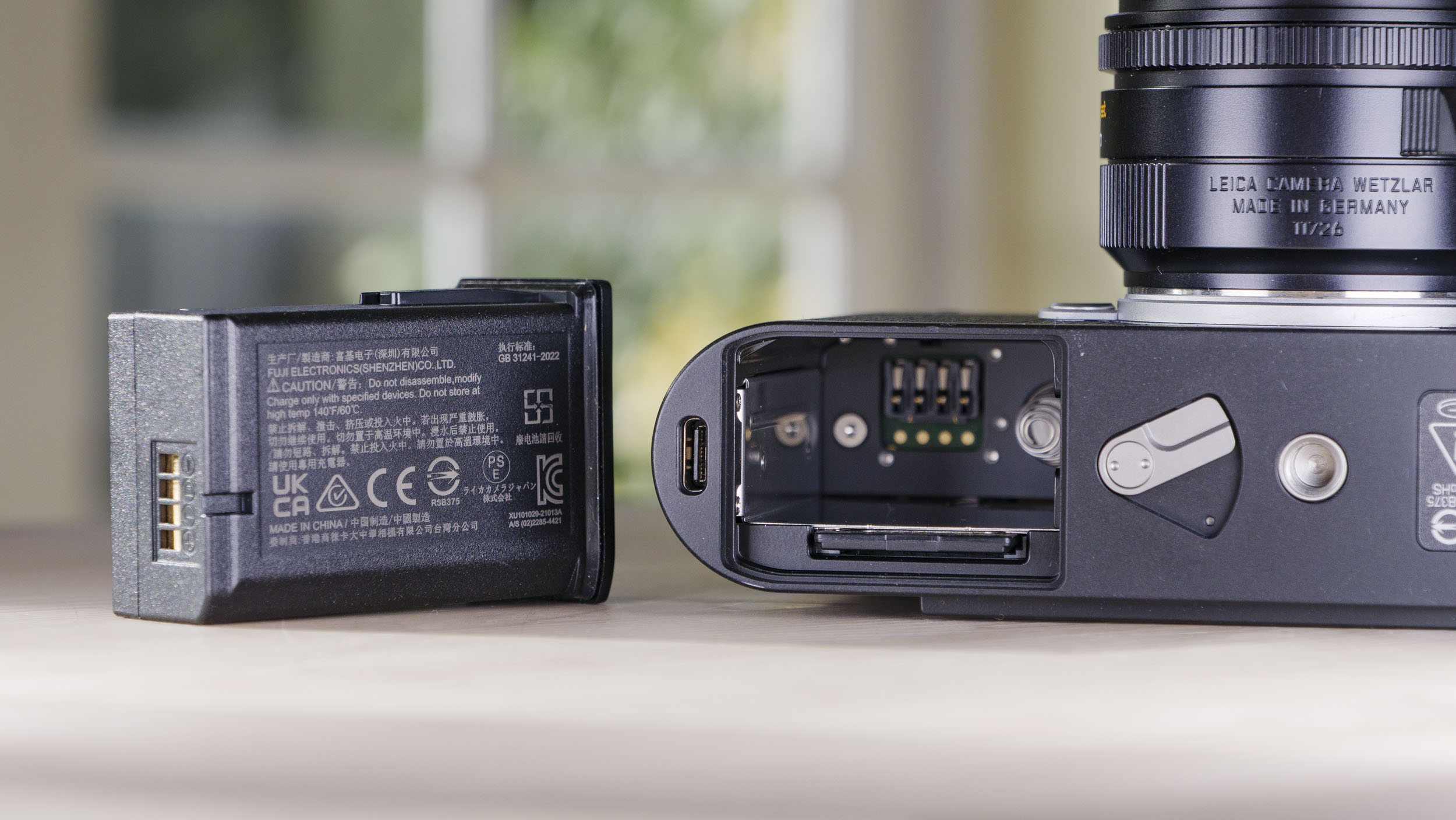 Close up of the Leica M EV1 camera's battery door, battery removed and placed next to the camera