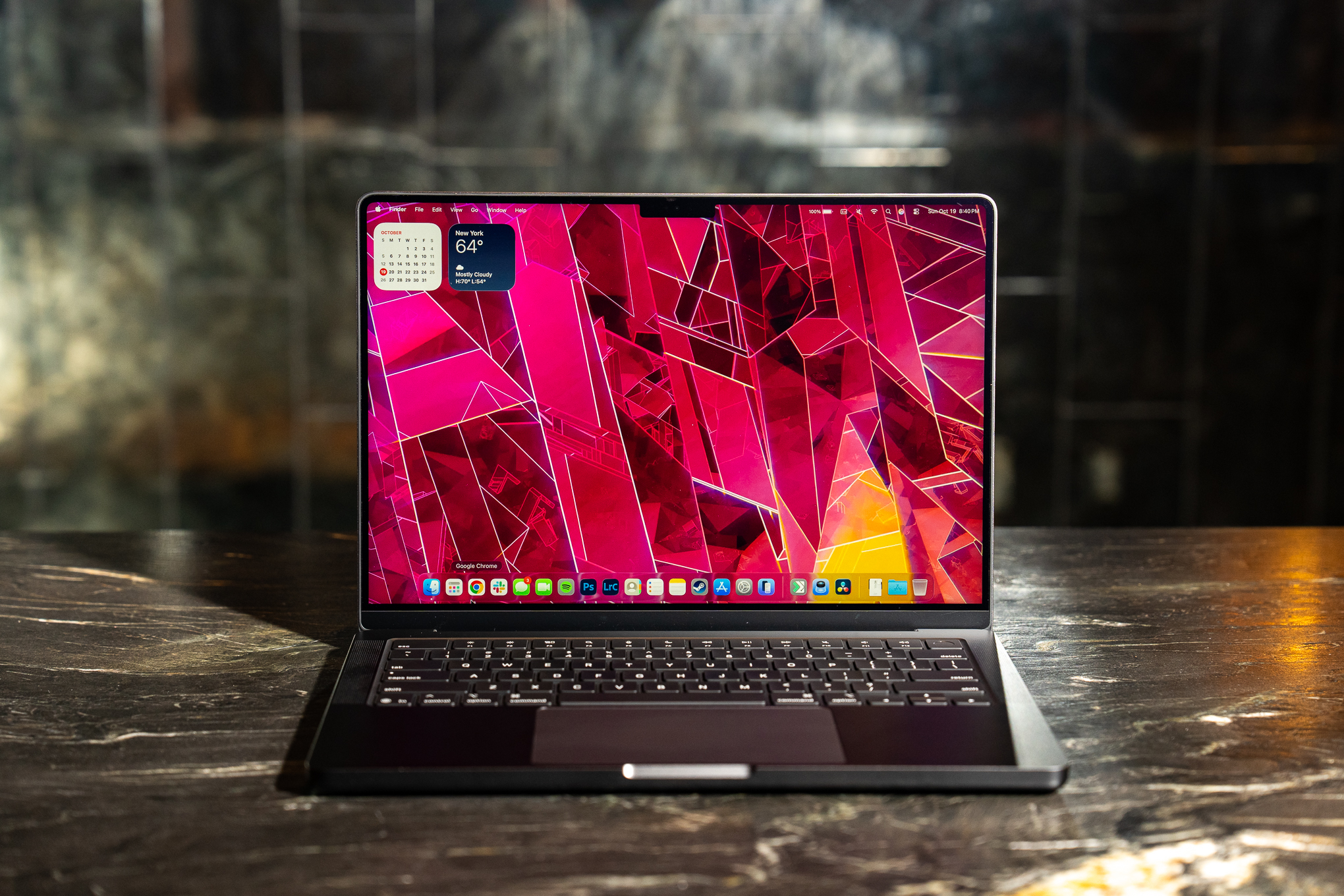A 2025 14-inch MacBook Pro M5 on a marble bar top with a dark mirrored reflection behind it.