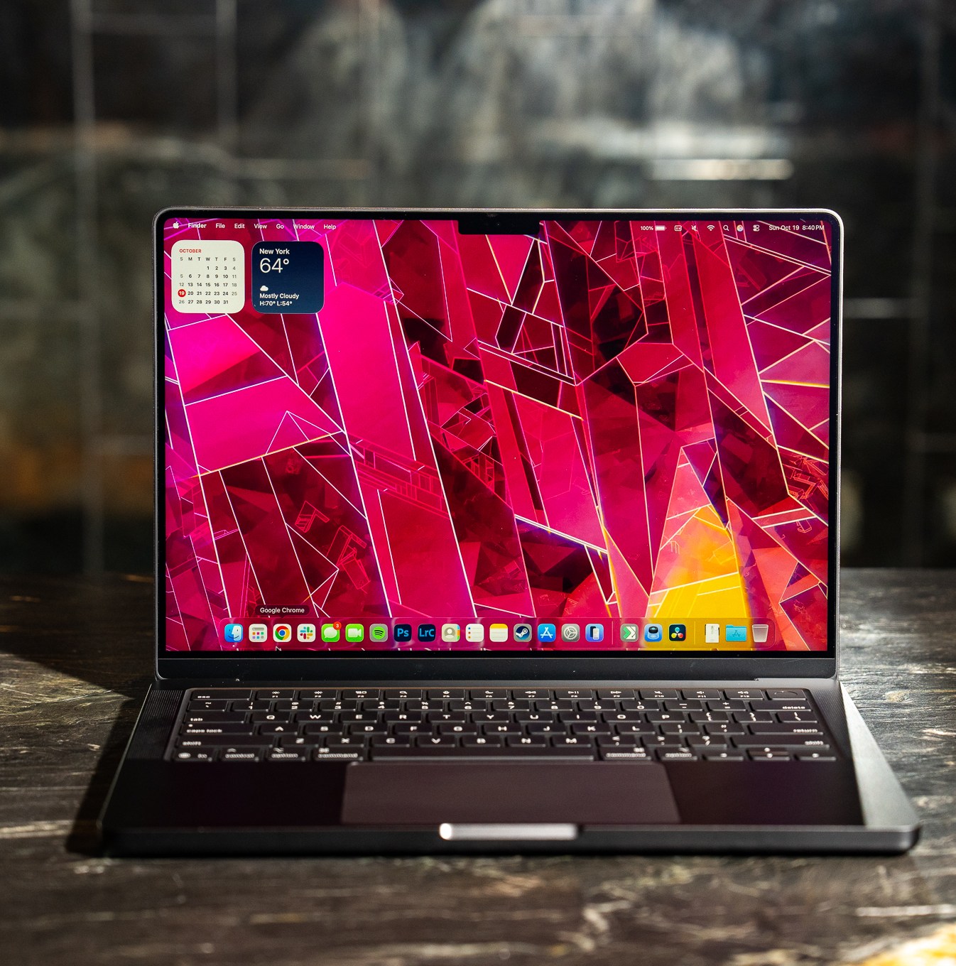 A 2025 14-inch MacBook Pro M5 on a marble bar top with a dark mirrored reflection behind it.