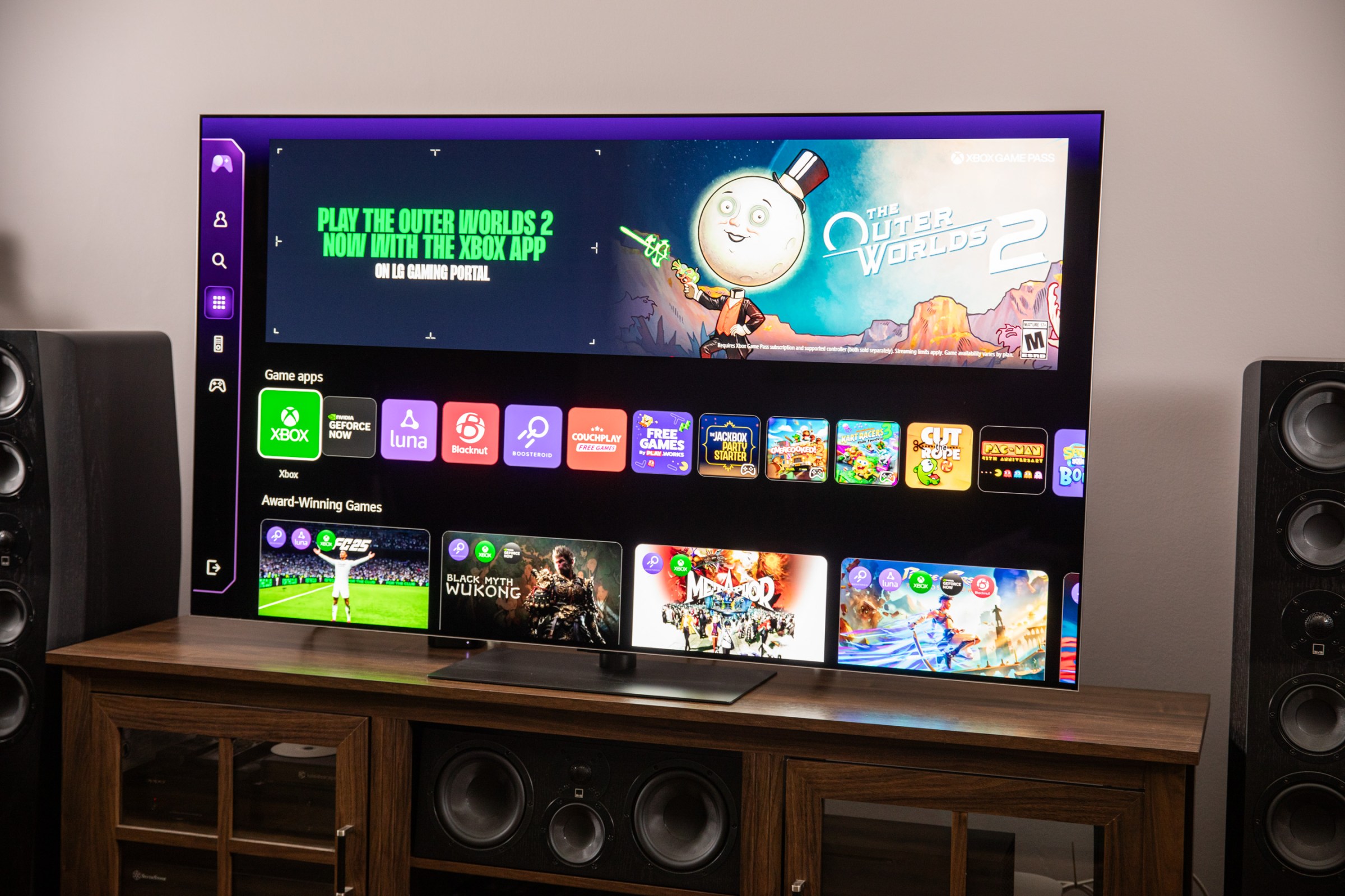The LG G5 on a wooden home theater credenza displaying the gaming OS screen.