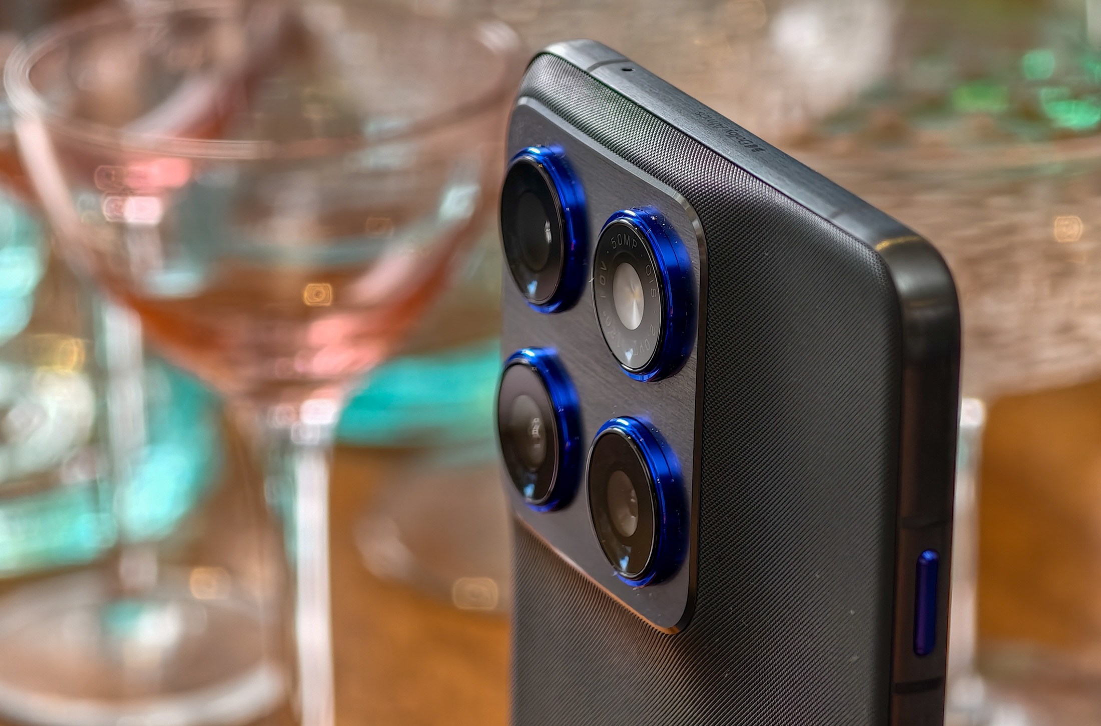 Photo of Motorola Edge 70 standing on a wooden table in front of cocktail glasses, showing the cameras
