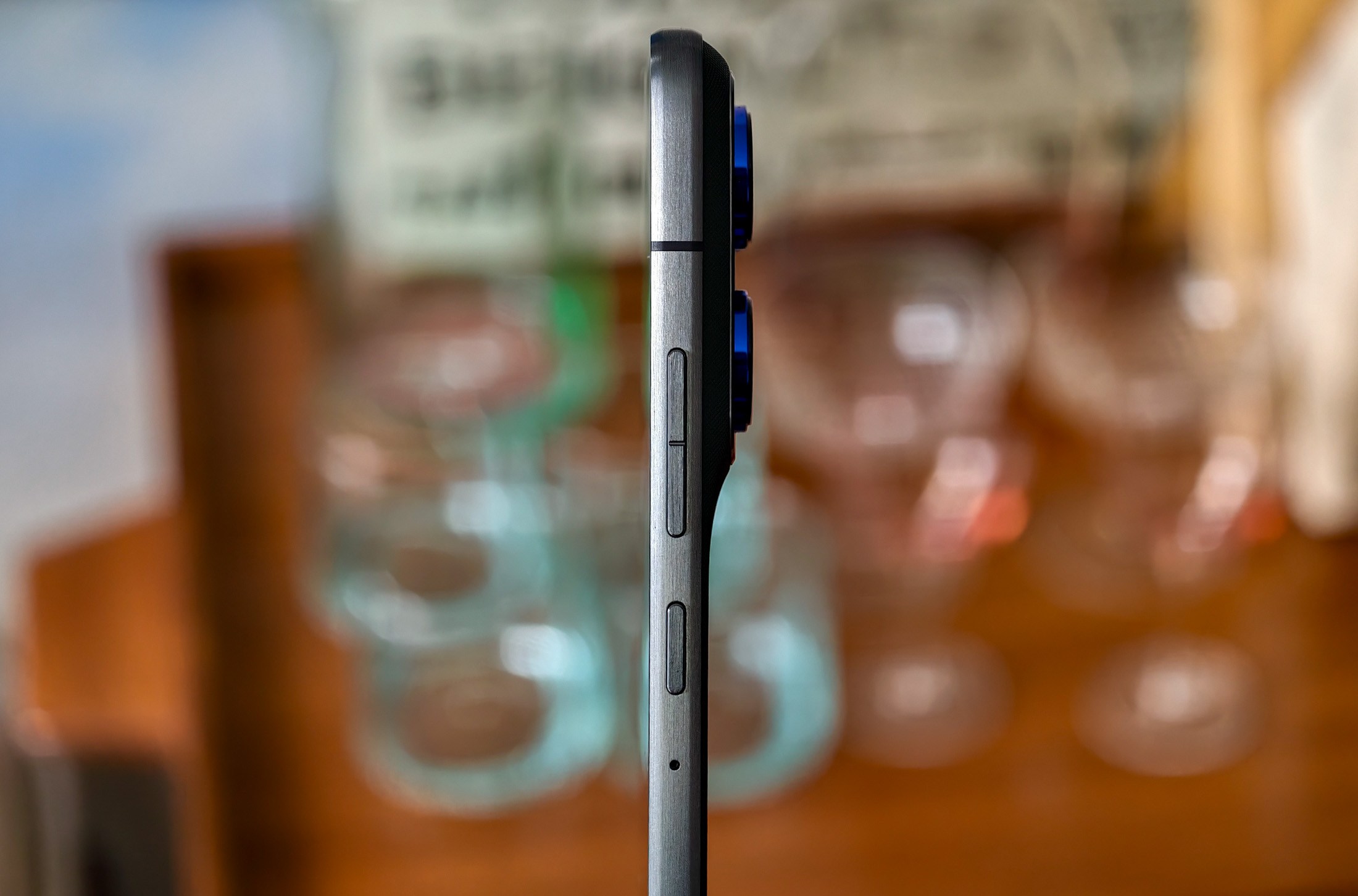 Photo of Motorola Edge 70 standing on a wooden table in front of some glasses, showing how thin the phone is
