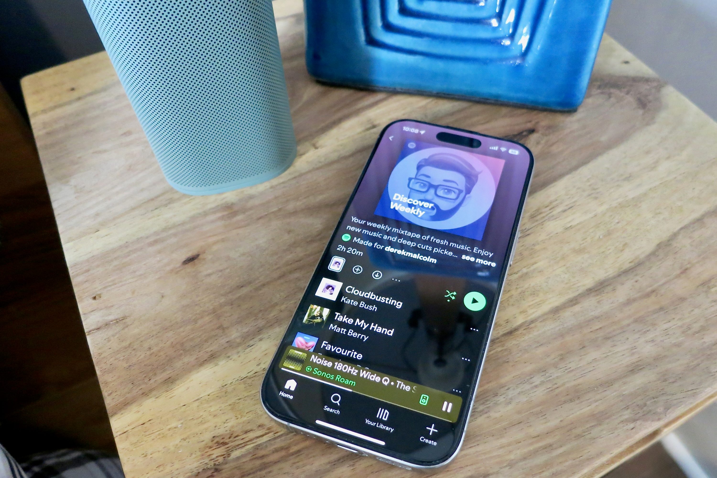 An iPhone sitting on a bedside table with the Discover Weekly playlist on its screen.