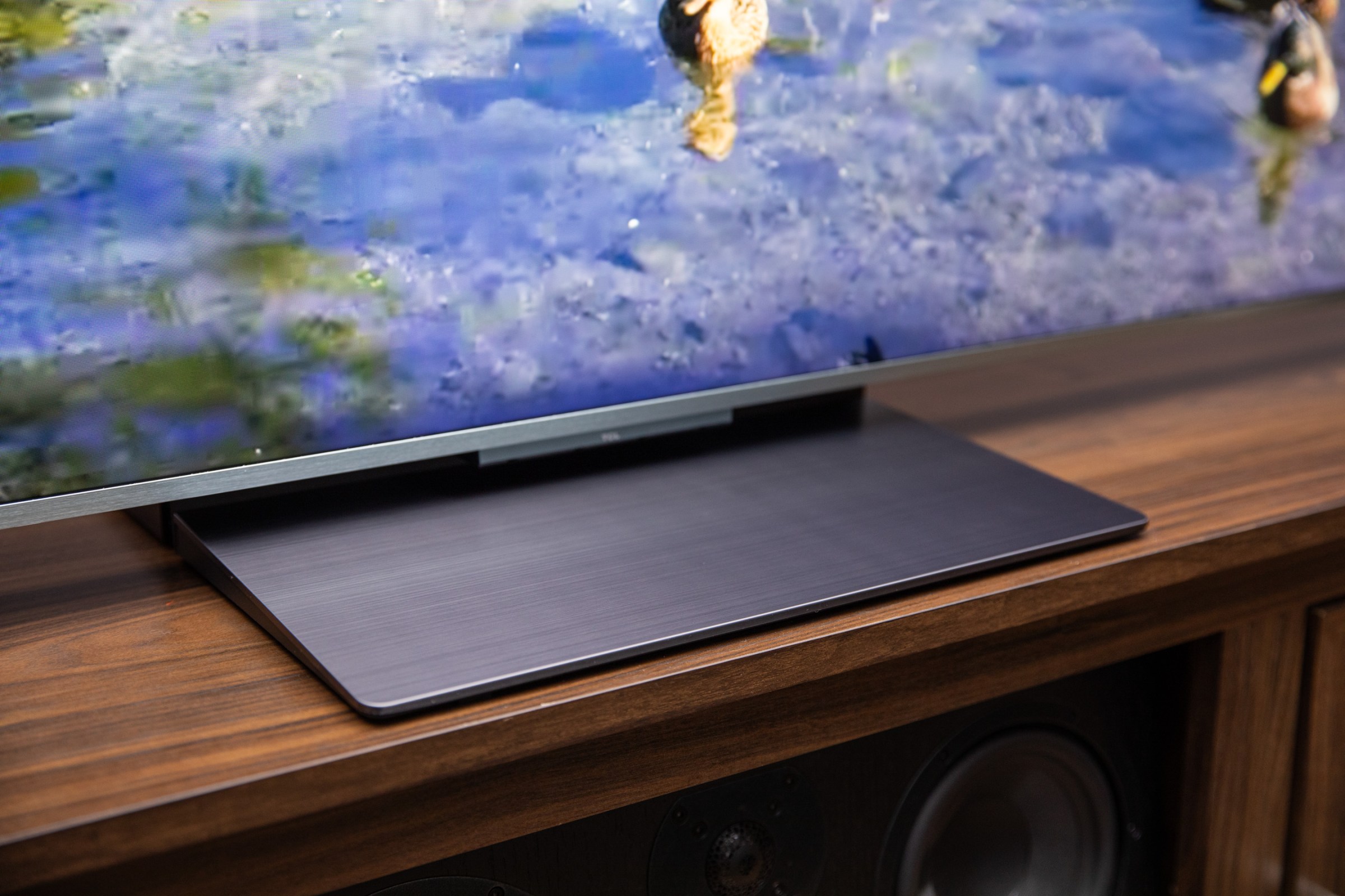 A closeup of the stand on the TCL QM9K TV on a wooden home theater credenza.