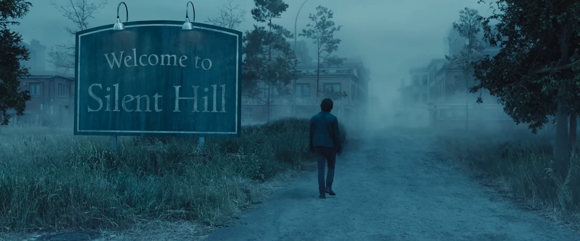 A man walking past a sign that reads Welcome to Silent Hill in the horror movie Return to Silent Hill.