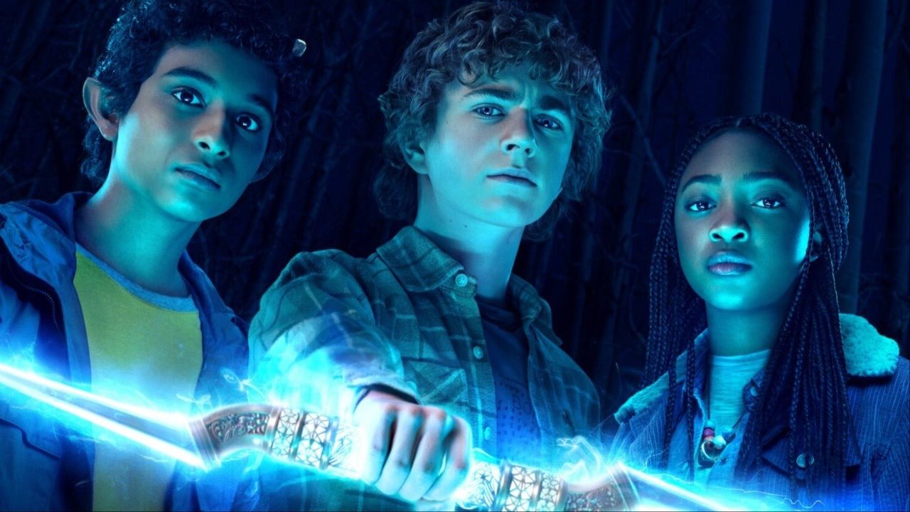 Three kids hold onto a glowing device with a lit blue background in the dark in a scene from Percy Jackson and the Olympians.
