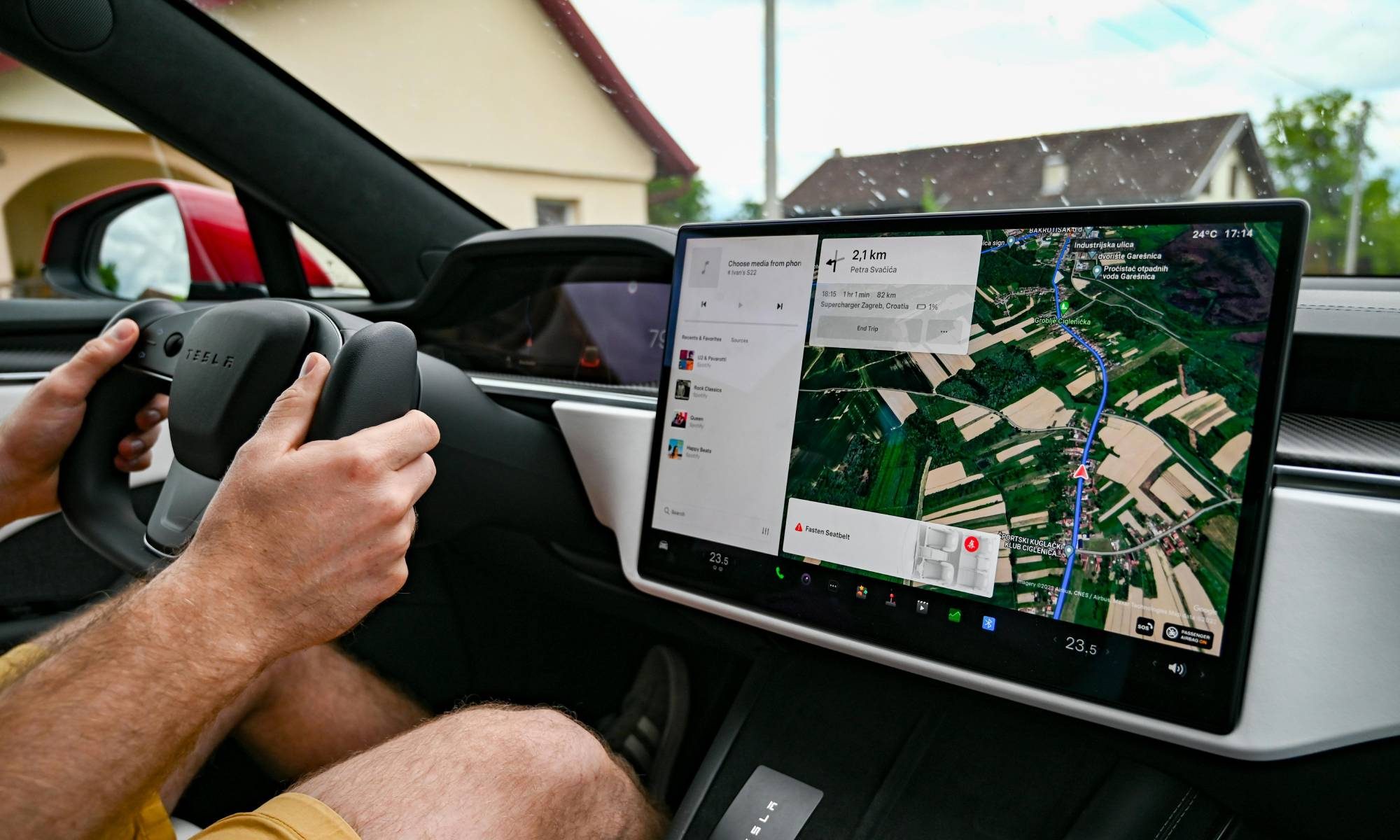 Person driving a Tesla with navigation on screen.