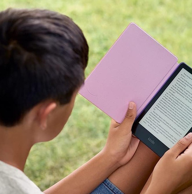Someone outside sitting in grass and reading on a Kindle Paperwhite Kids device