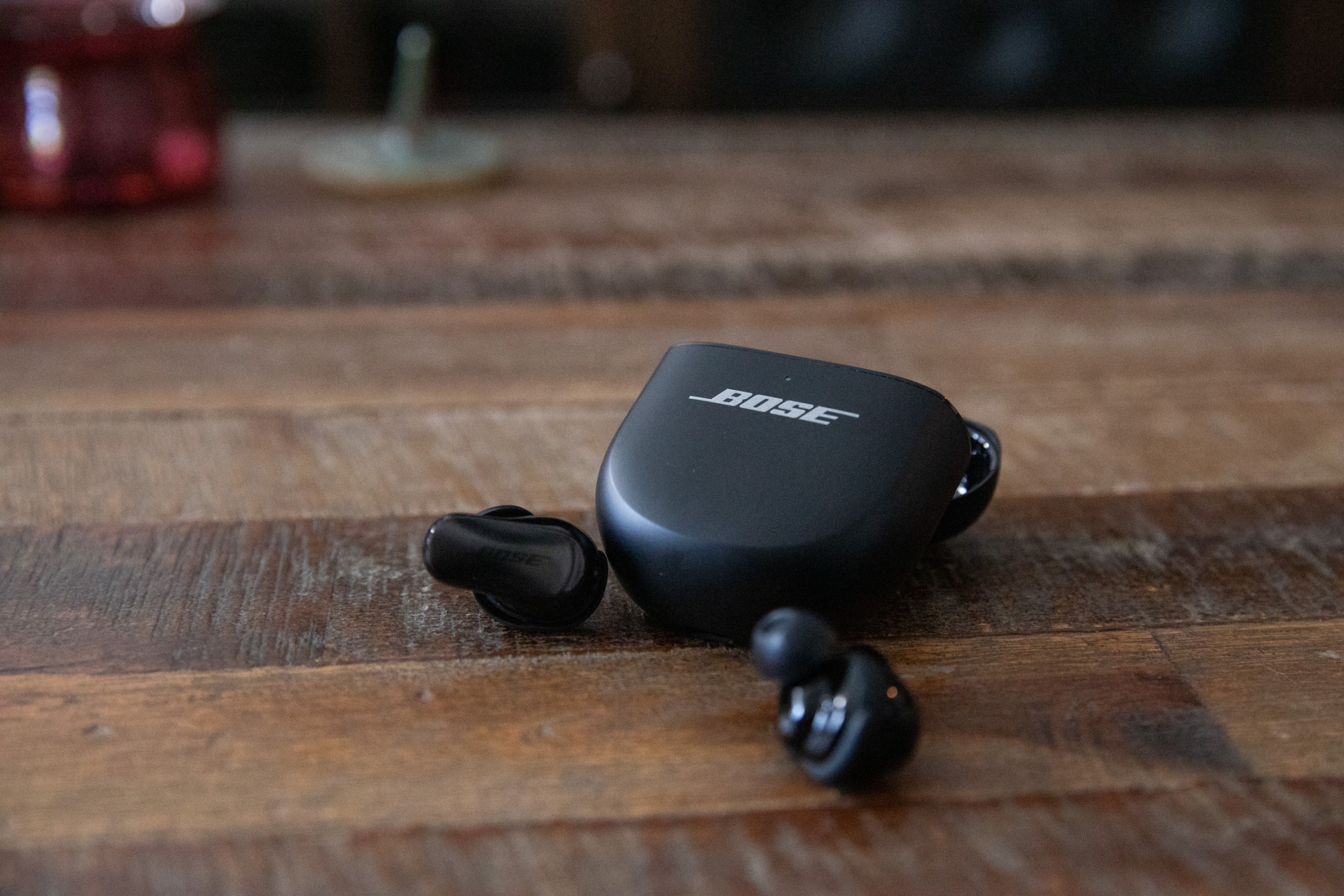 The Bose QuietComfort Ultra Earbuds Gen 2 next to their case on a wooden coffee table.