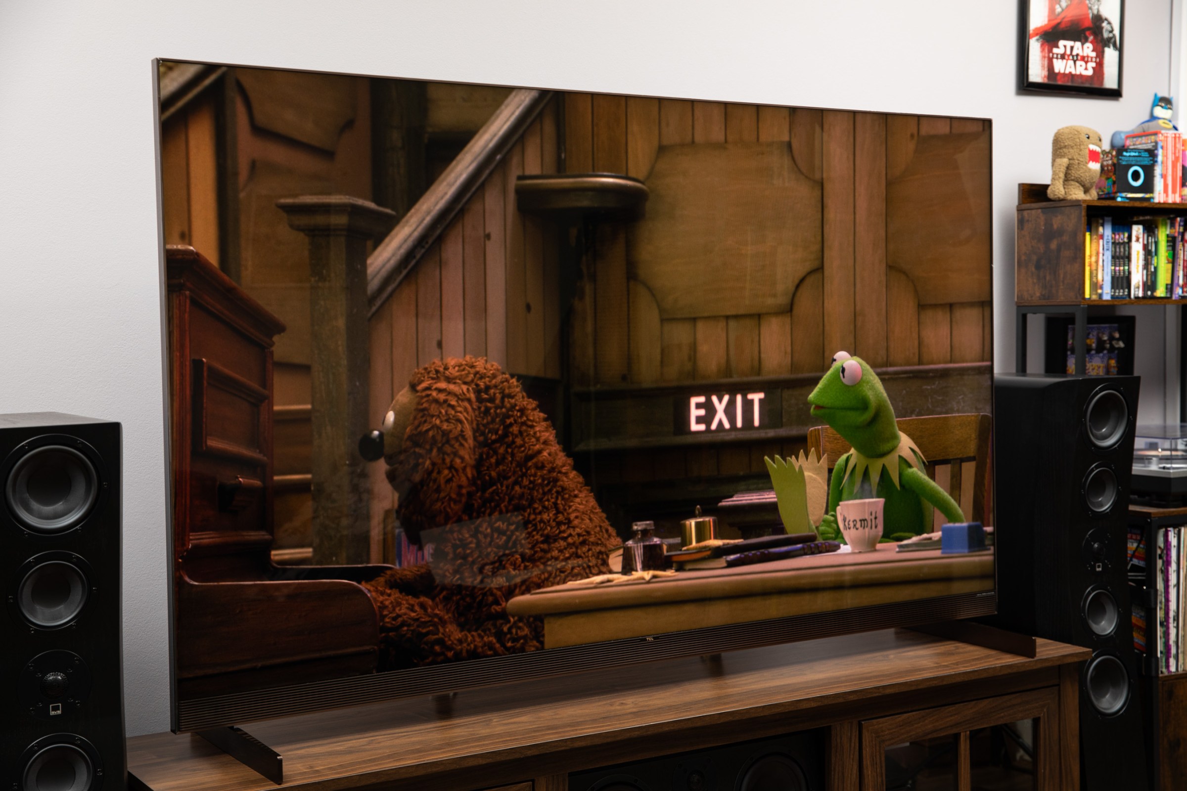 The TCL X11L displaying a scene with Rowlf and Kermit from The Muppet Show special on a dark wood TV stand.