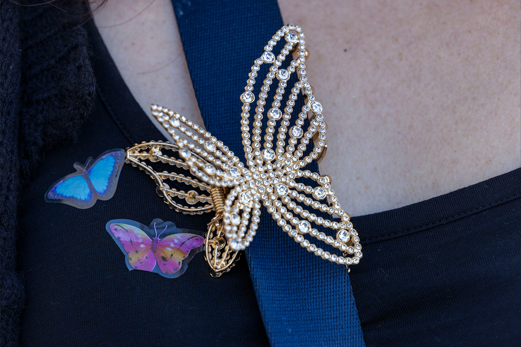 Closeup shot of a butterfly clip with rhinestones on a person’s bag strap.