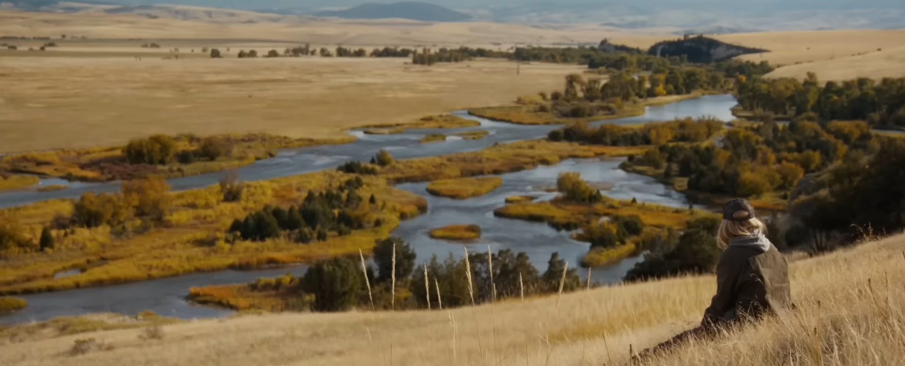 Michelle Pfeiffer sitting on a hill looking out at a valley in The Madison.