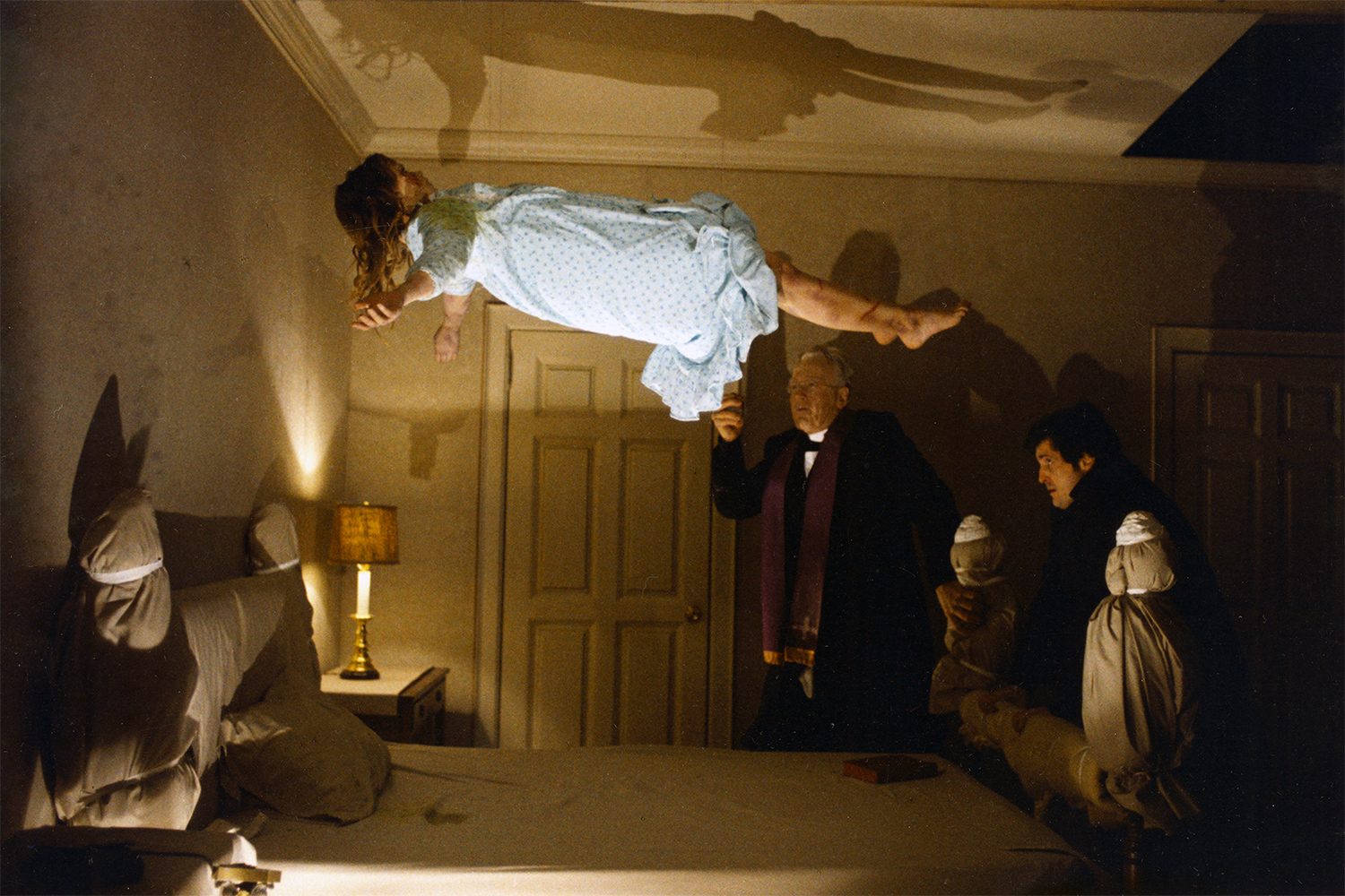 Regan MacNeil (Linda Blair) levitates above her bed in front of Damien Karras (Jason Miller) and Father Lankester Merrin (Max von Sydow) in The Exorcist.