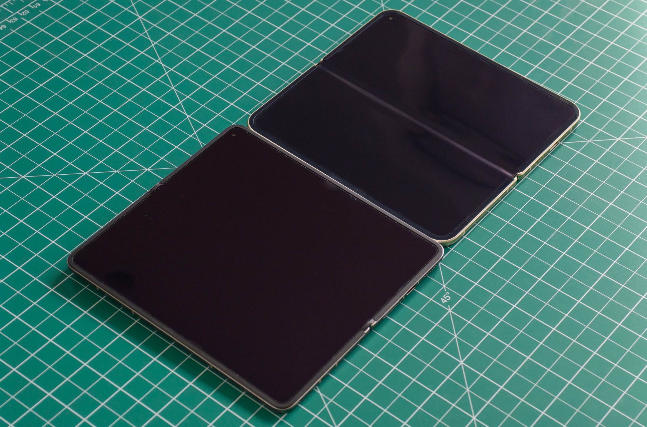 Photo of Oppo Find N6 and Google Pixel 10 Pro Fold side by side on a green work mat from above at an angle, with the screens open and off, showing a much more visible crease on the Pixel