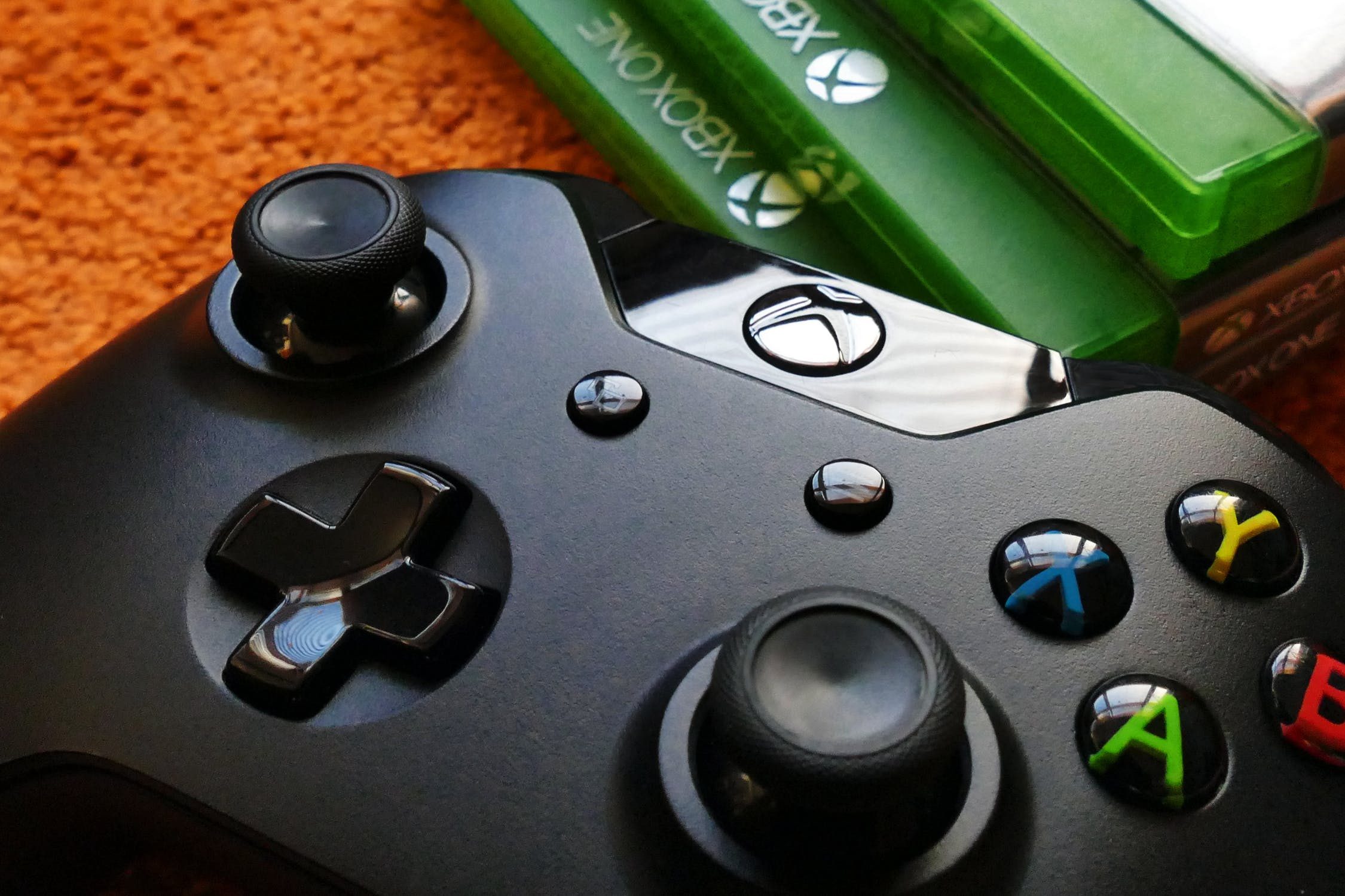 An Xbox controller sits on a floor next to a stack on Xbox One games.