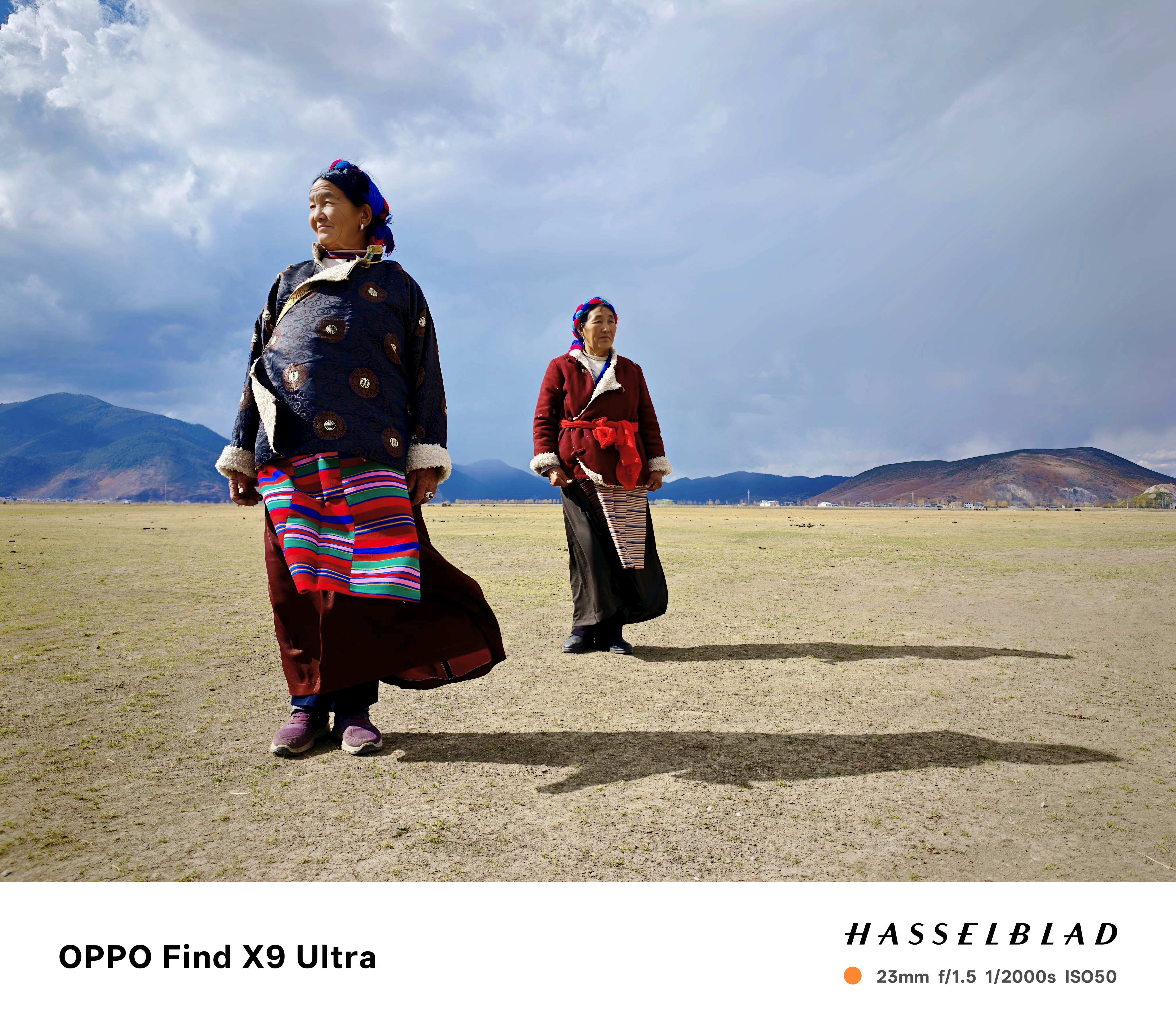 Two women in traditional Tibetan clothing standing on a plain, with their shadows