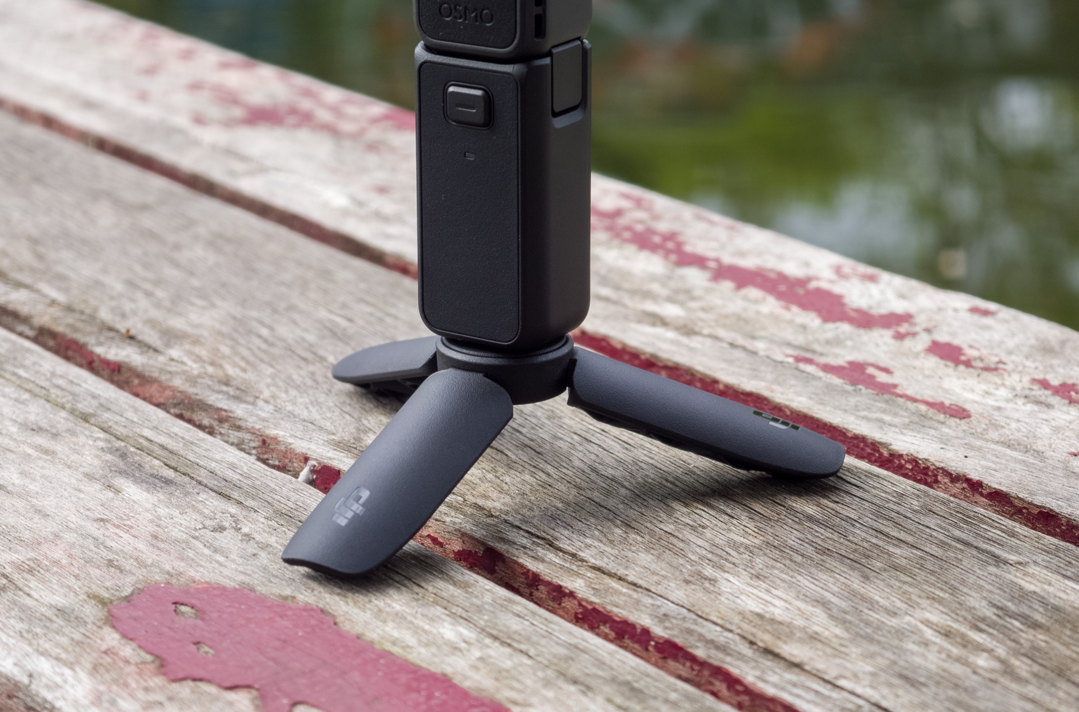 Photo of the DJI Osmo Pocket 4 tripod on a wooden table in front of a canal