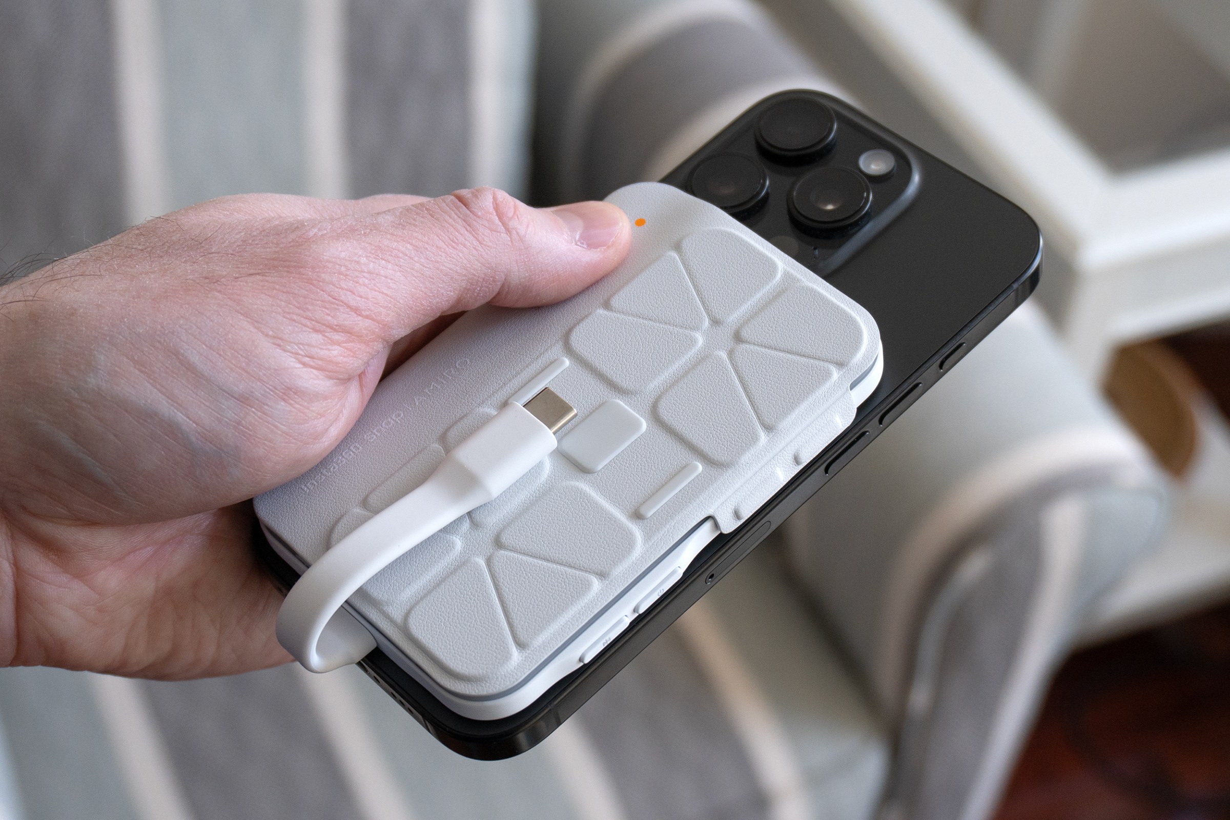 A person holds an iPhone in one hand with the Insta360 Snap screen accessory attached and its screen cover closed.