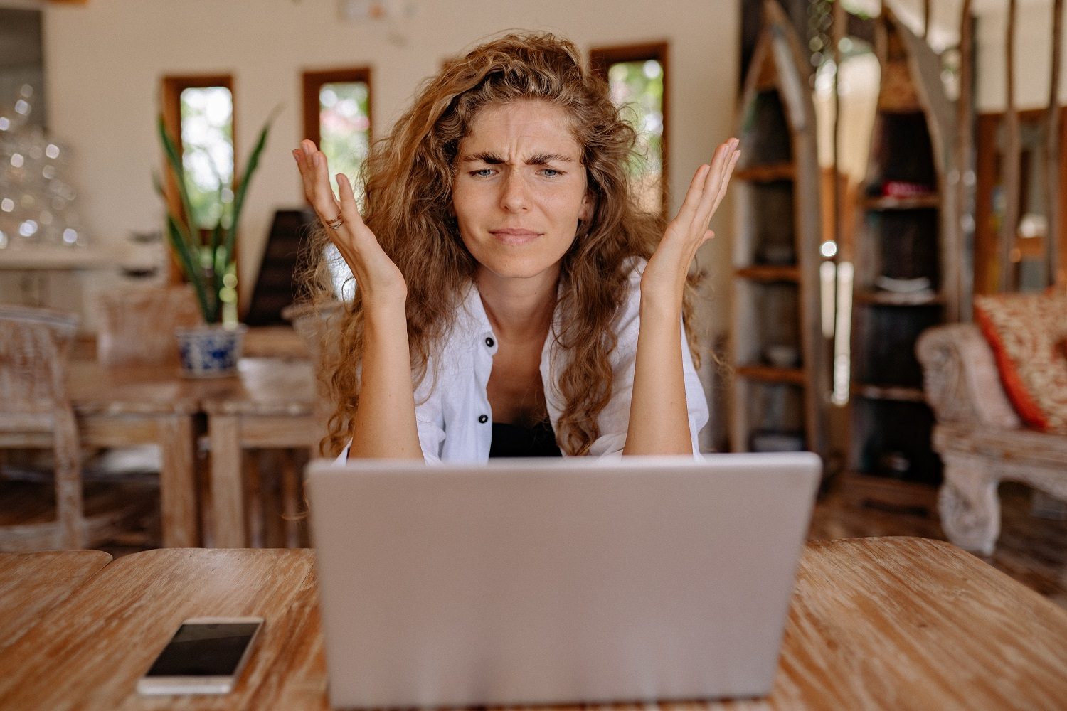 A person looking frustrated at a laptop while sitting at a table.
