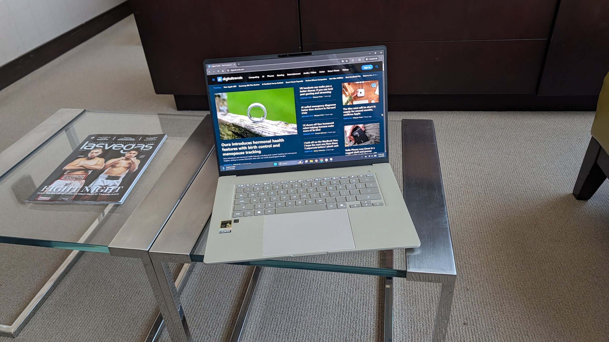 Asus Zenbook A16 open on a glass coffee table, showing the digital trends homepage