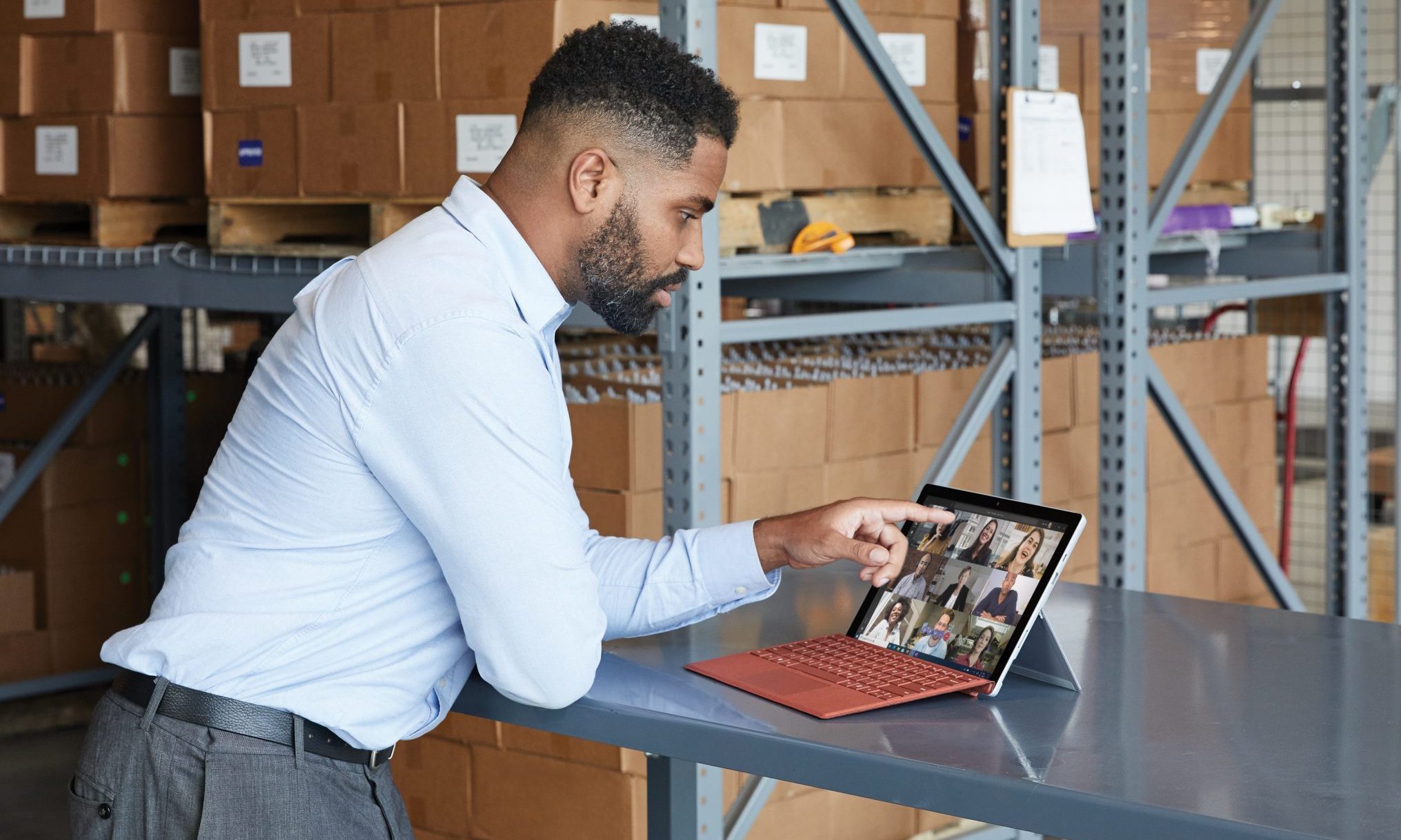 A man standing in a warehouse using a Surface Tablet to make a Teams video call