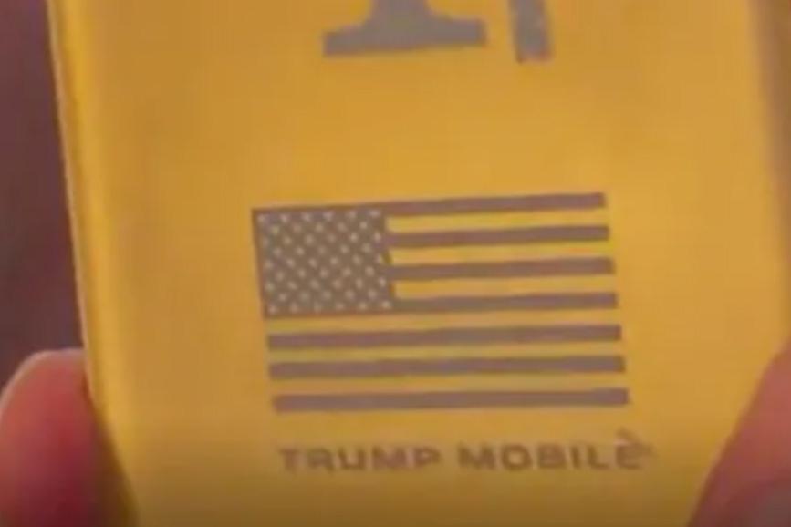 A still from The Verge’s video interview with Trump Mobile staff showing the T1 Phone with 13 stripes on the US flag logo.