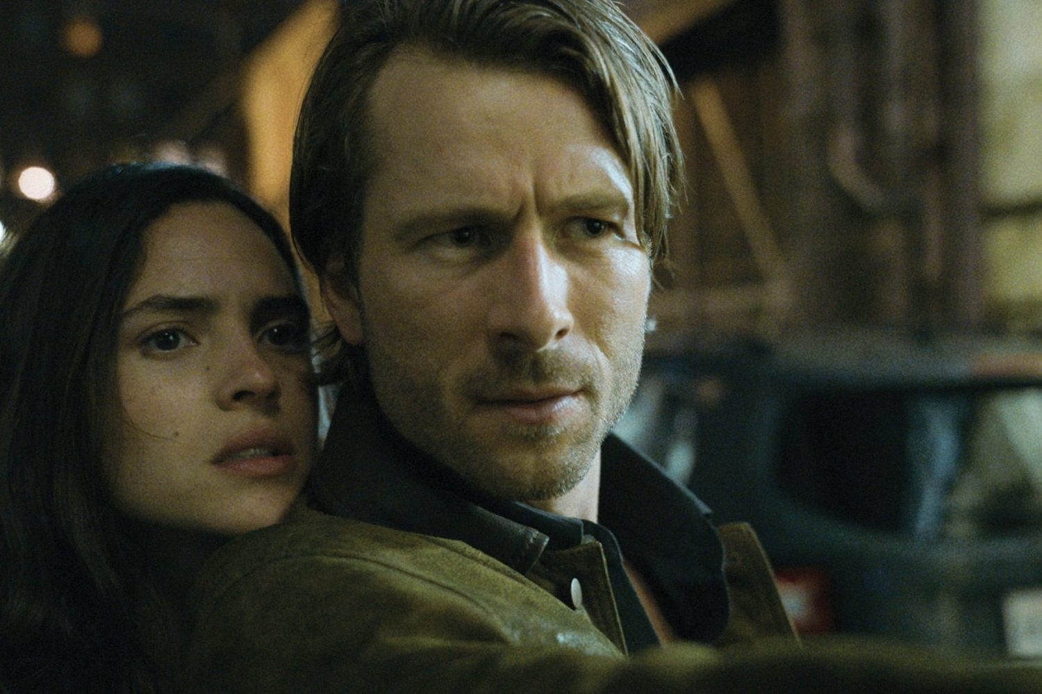A woman rests her head on a man's shoulder while he poits a gun.