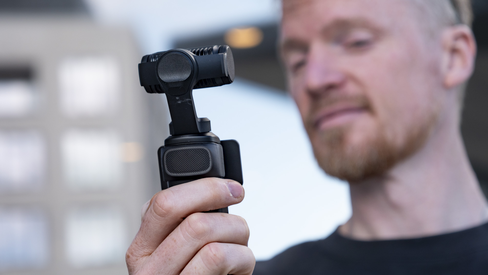 Man holding the Insta360 Luna Ultra vlogging camera, outdoors in a grey urban scene