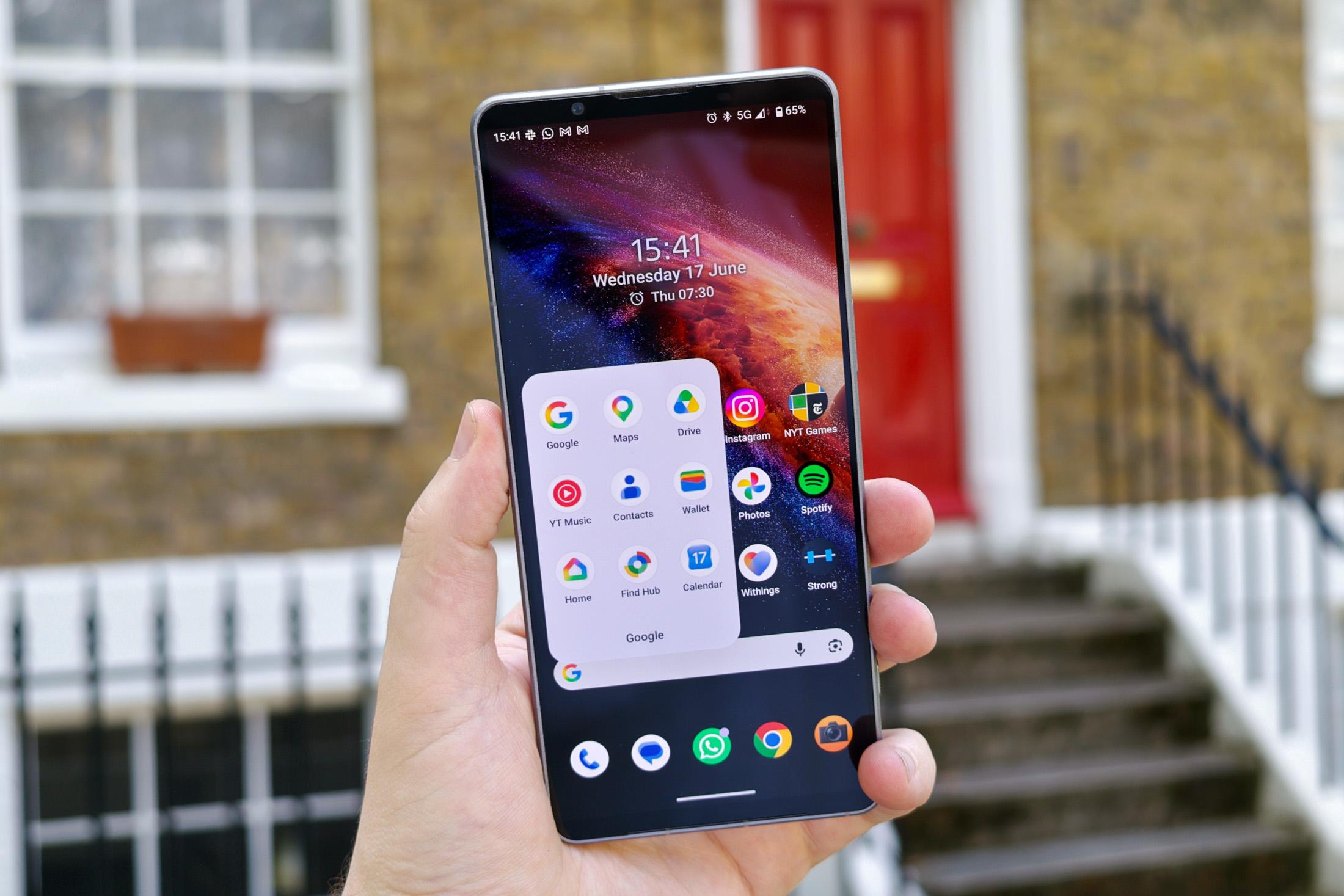 Photo of the Sony Xperia 1 VIII in front of a house, showing the homescreen and an app icon folder