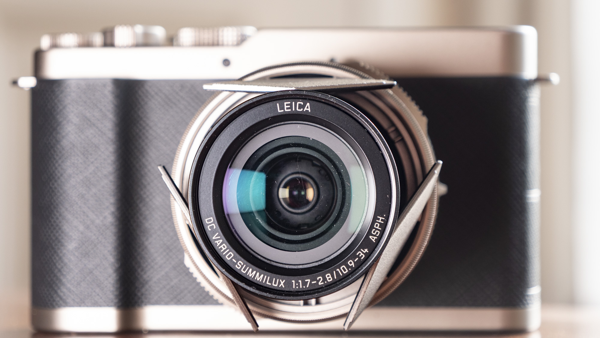 Close up of the lens, of the Titanium Gold special edition of the Panasonic Lumix L10 compact camera, on an antique wooden table 