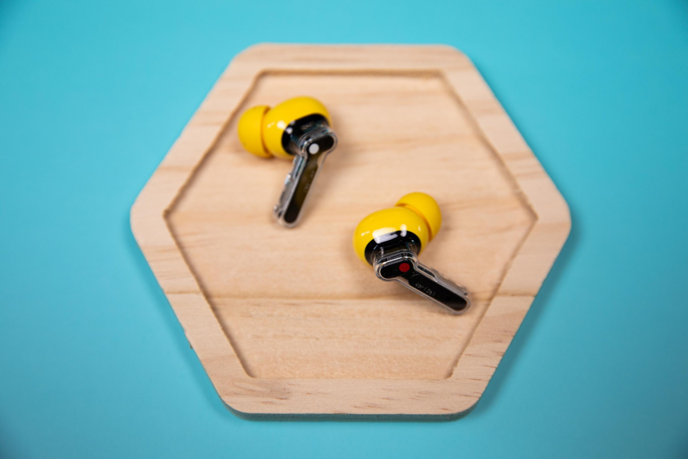 The Nothing Ear 3A earbuds on a wooden hexagon plate with a teal background.